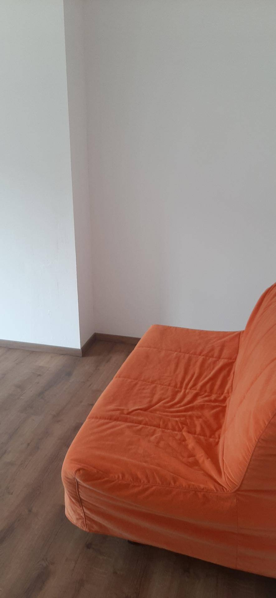 Nahaufnahme eines orangefarbenen Sofas in einem hellen Raum mit Holzboden und weißen Wänden.