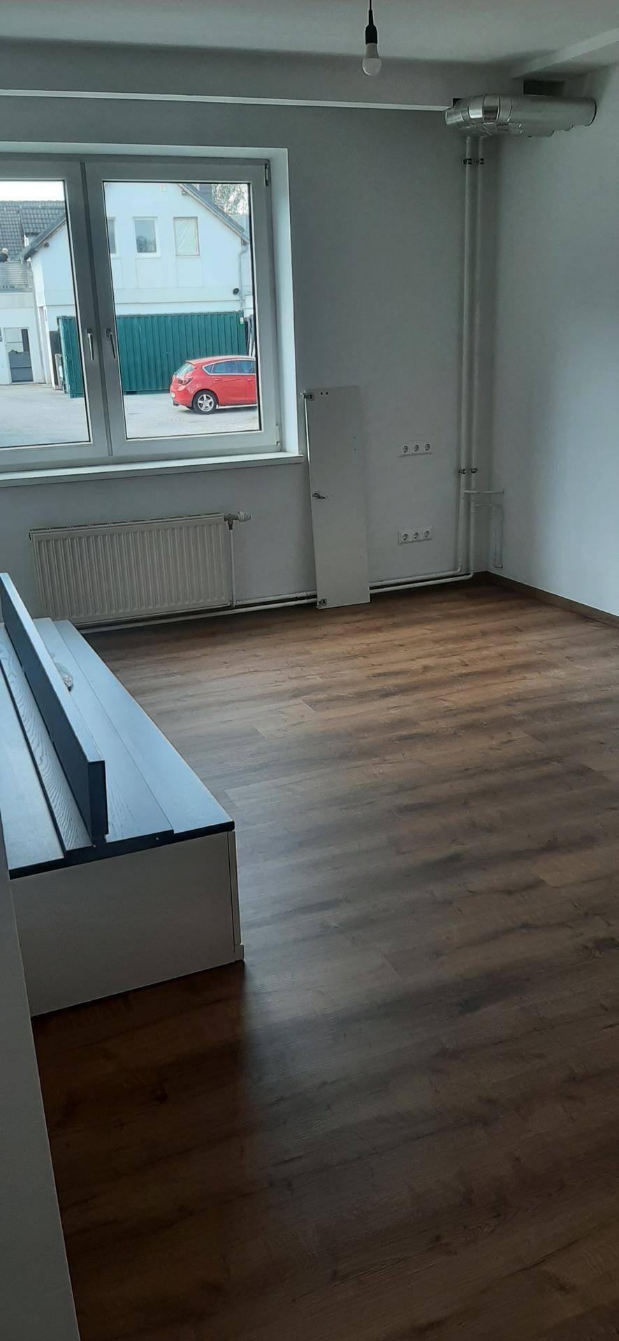 Heller Raum mit großem Fenster, Blick nach draußen und einer langen weißen Sitzbank mit Stauraum.