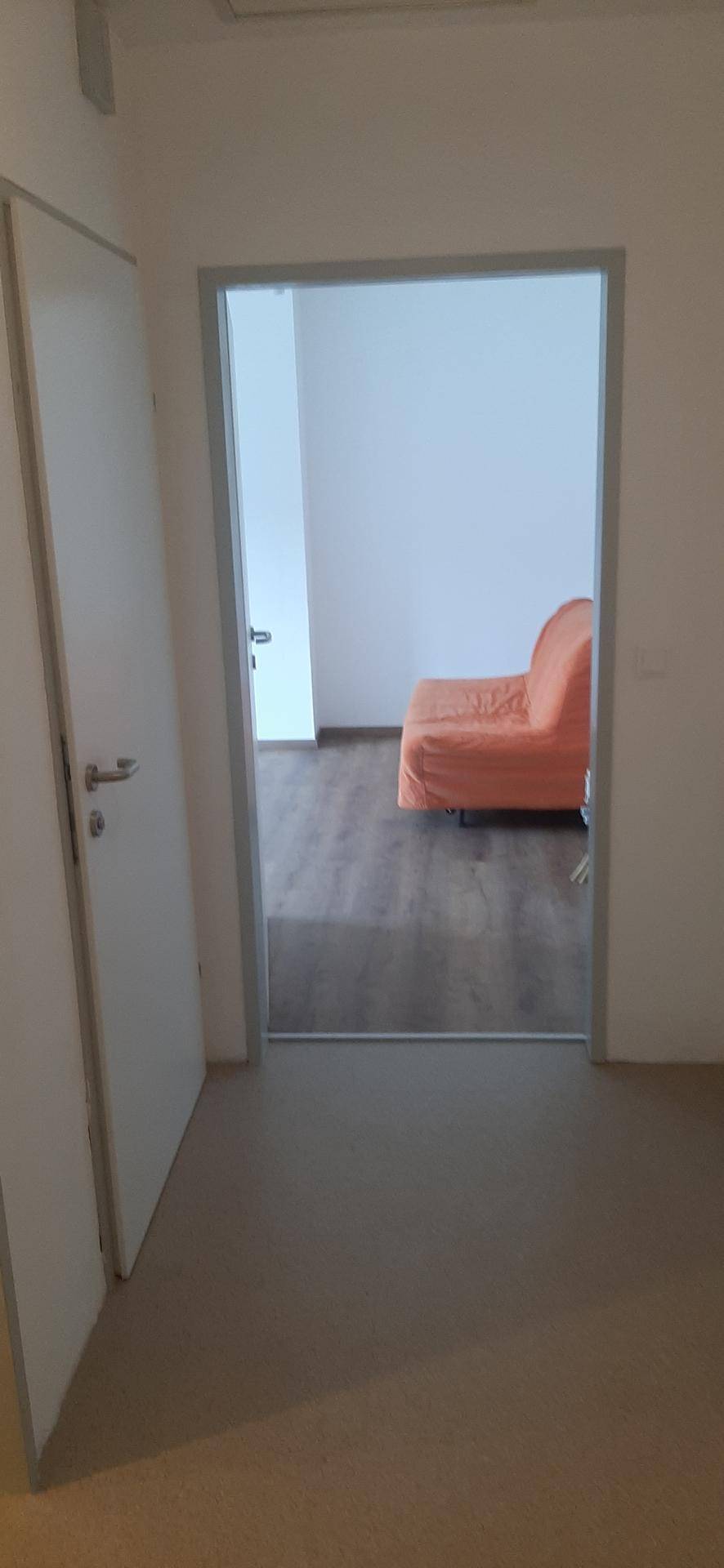 Blick durch eine Tür in ein helles Zimmer mit einem orangefarbenen Sofa und Holzboden.