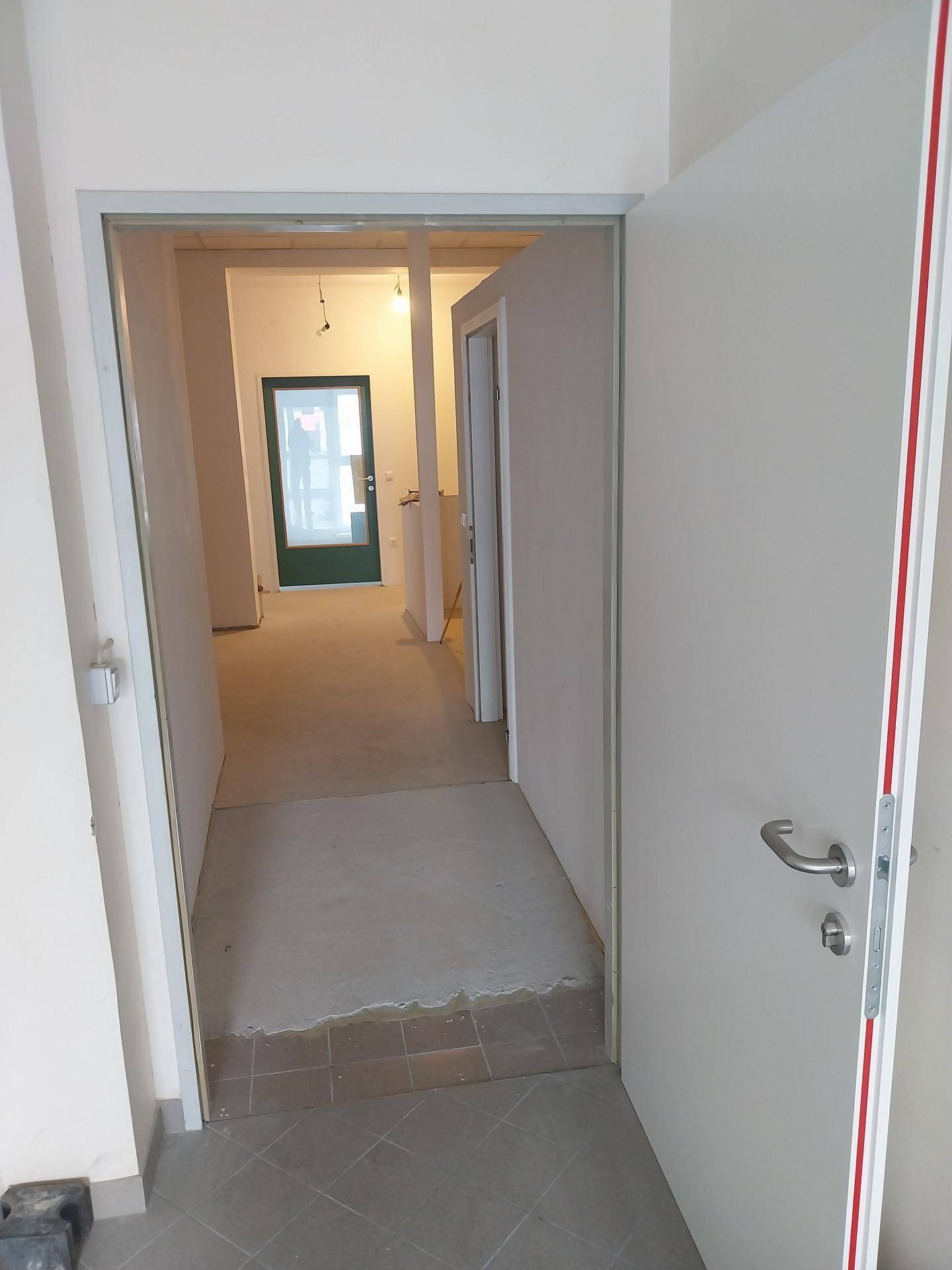 Flur im Bau mit offener Tür, Blick in weitere Räume und provisorischem Boden.