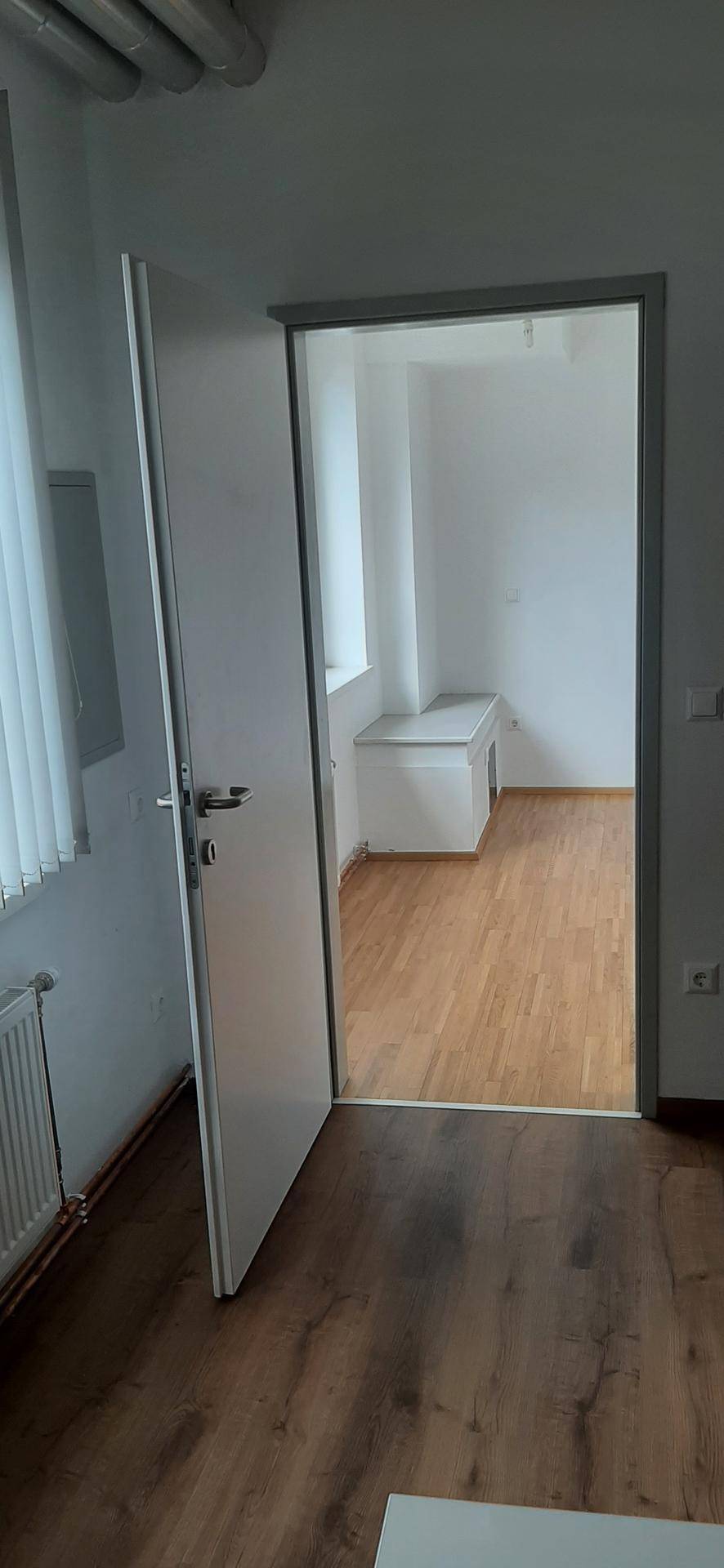 Blick durch eine offene Tür in ein helles Büro mit Fenster, Heizkörper und weißer Ablagefläche.