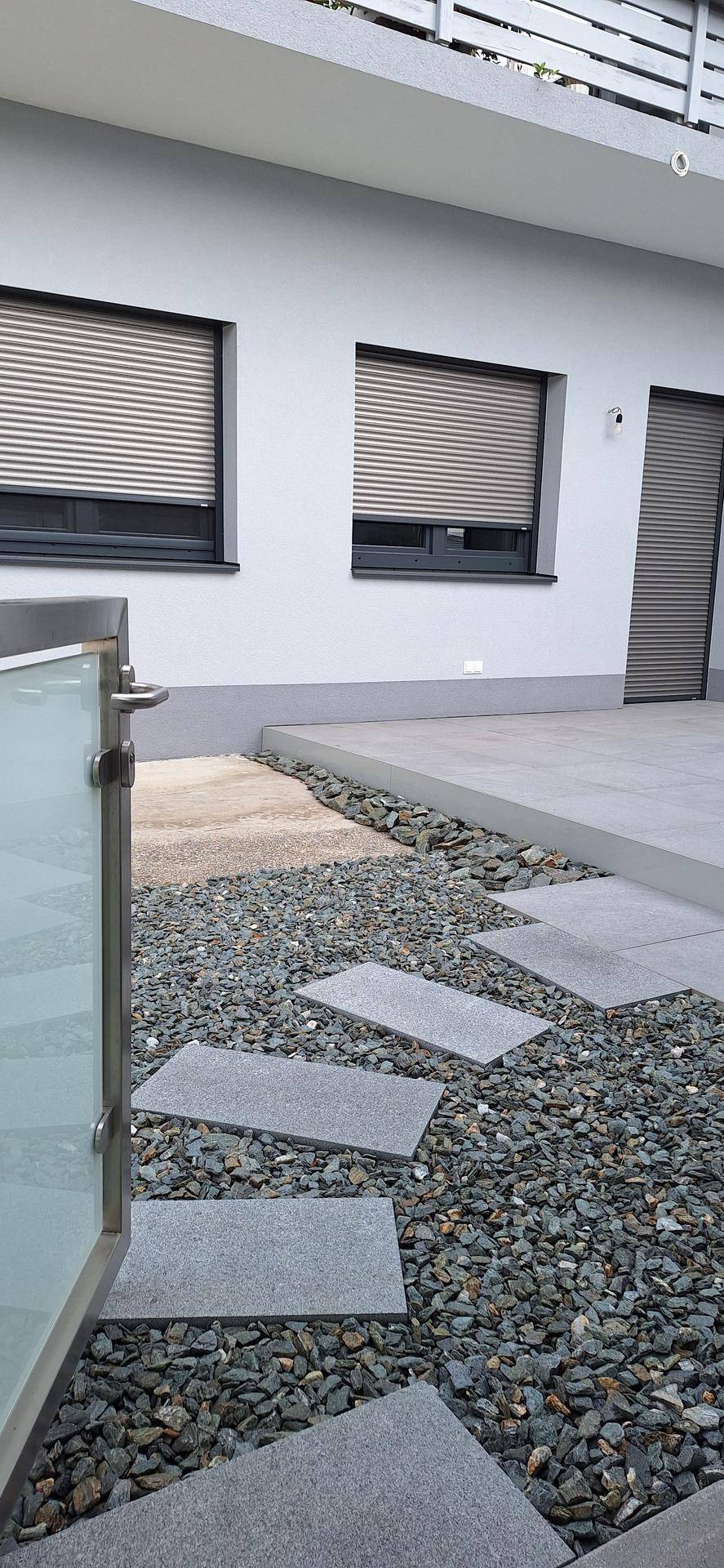 Seitenansicht des modernen Gebäudes mit geschlossenen Rollläden an den Fenstern und einem Kiesweg.