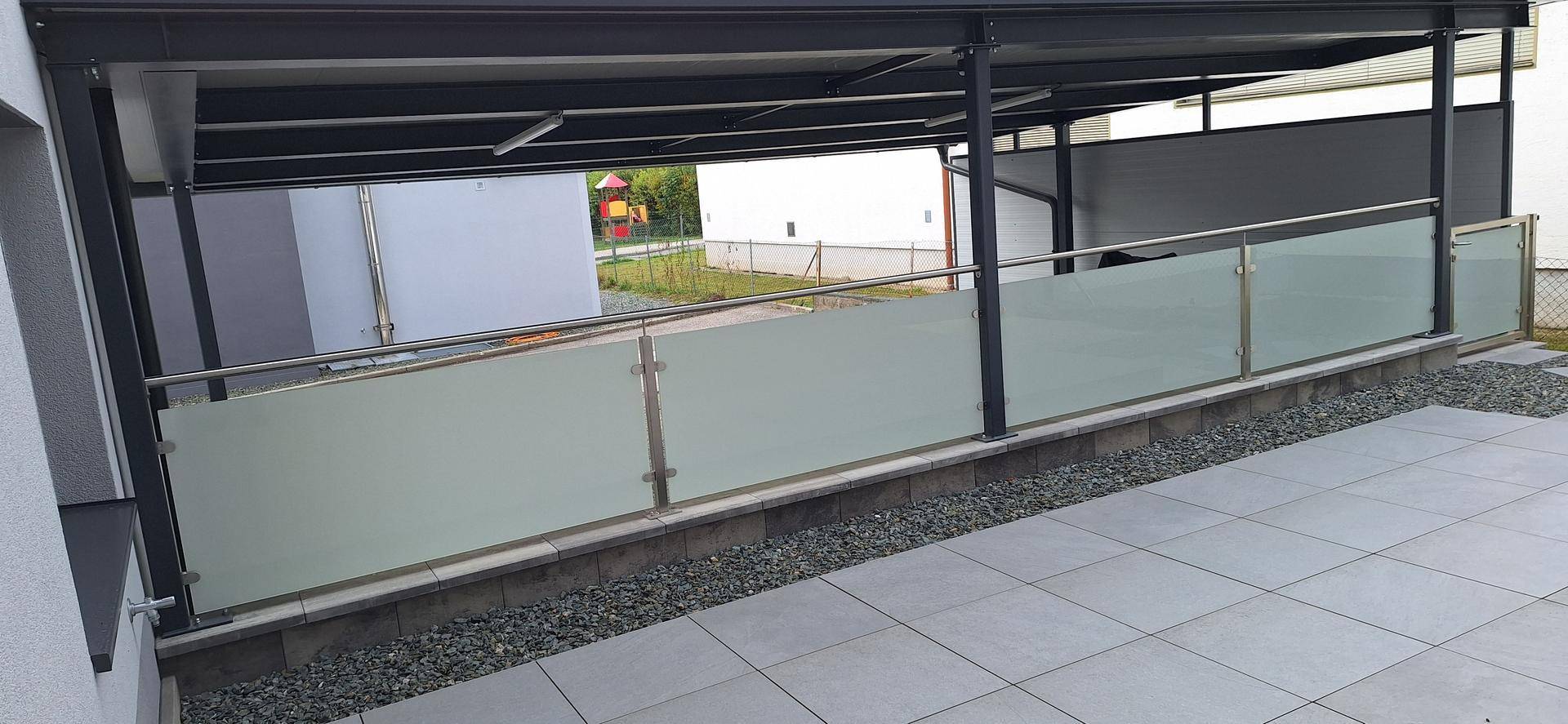Moderne Terrasse mit Fliesenboden, Glasgeländer und Kiesbeet, ideal für entspannte Stunden im Freien.