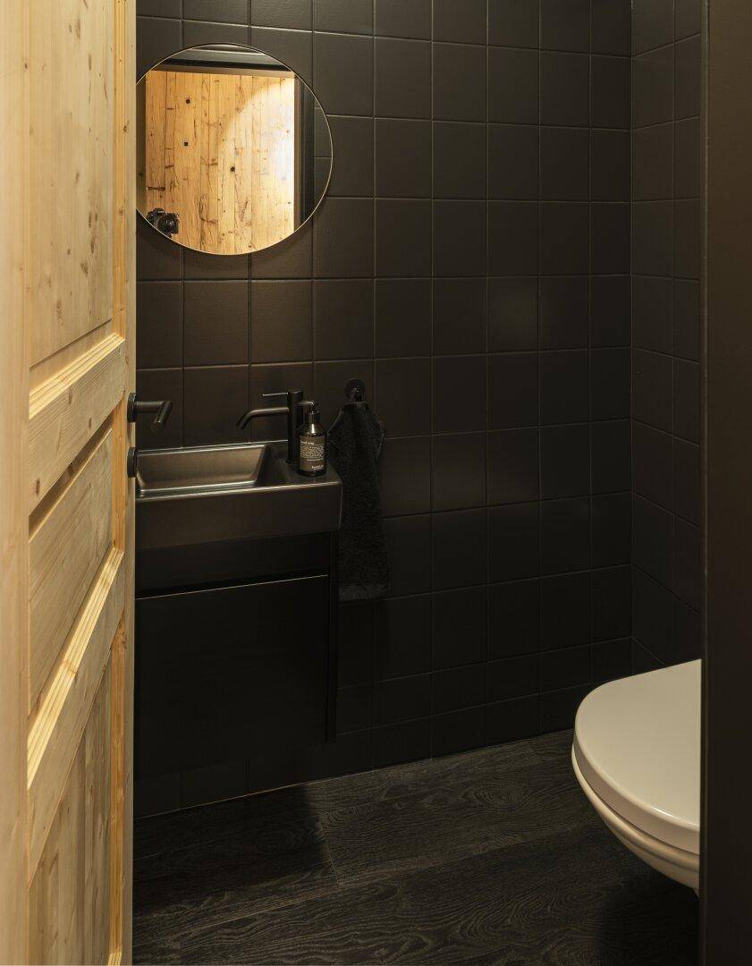 Modernes Gäste-WC mit schwarzen Fliesen, kleinem Waschbecken und dunklem Holzboden.