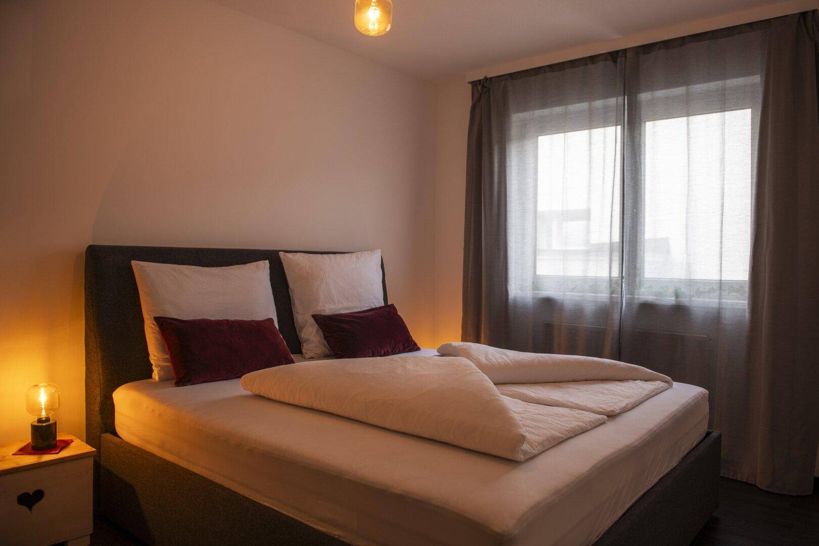 Gemütliches Schlafzimmer mit Doppelbett, Nachttischlampe und dunklen Vorhängen für entspannte Abende.