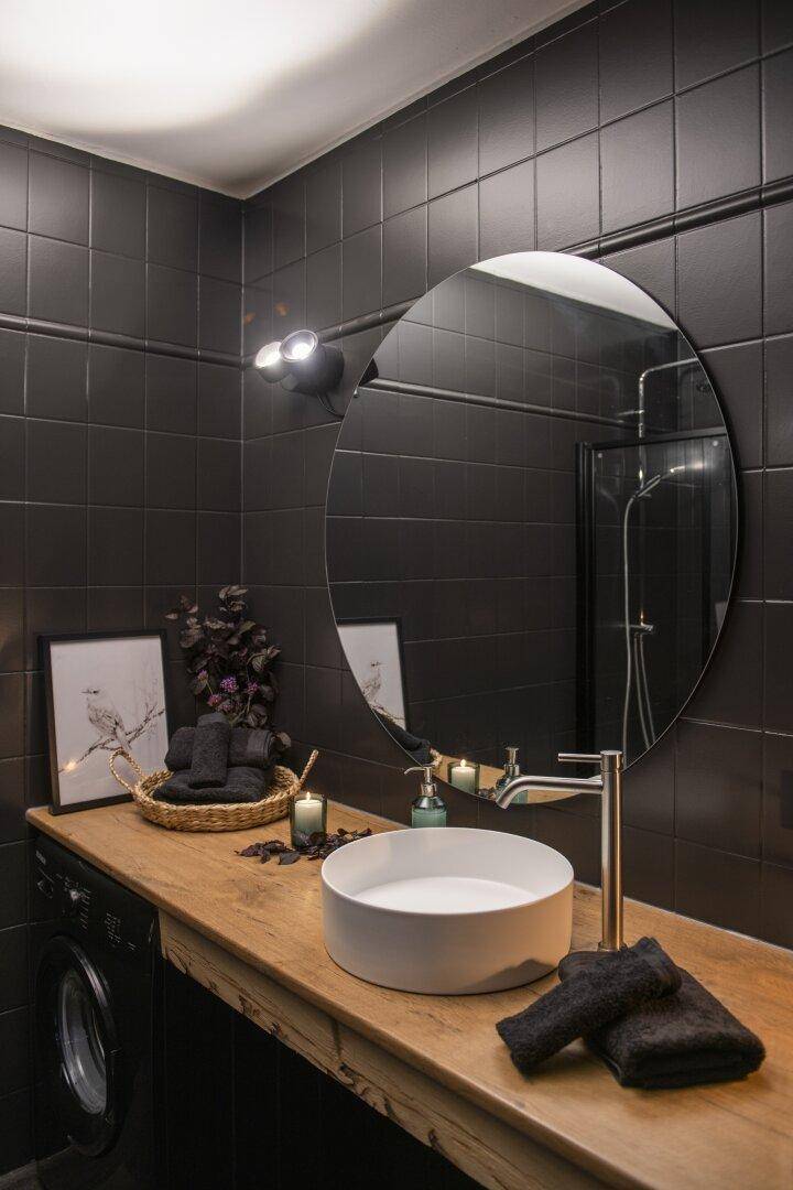Modernes Badezimmer mit schwarzen Fliesen, Holzwaschtisch und Aufsatzwaschbecken, inklusive Waschmaschine.