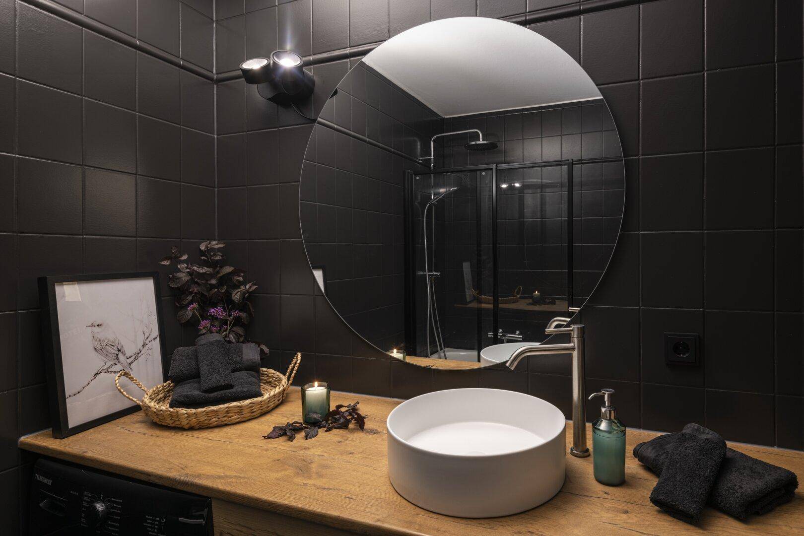 Detailansicht des modernen Badezimmers mit rundem Spiegel, Aufsatzwaschbecken und Duschbereich.