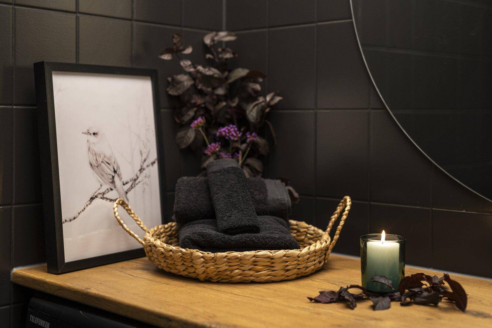 Dekorative Elemente im modernen Badezimmer: Korb mit Handtüchern, Kerze und gerahmtes Bild.