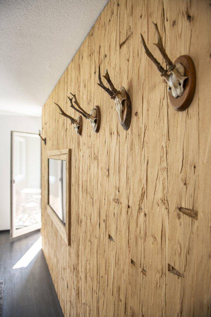 Langer Flur mit rustikalen Holzpaneelen und Geweihdekoration, der zu einem hellen Bereich führt.