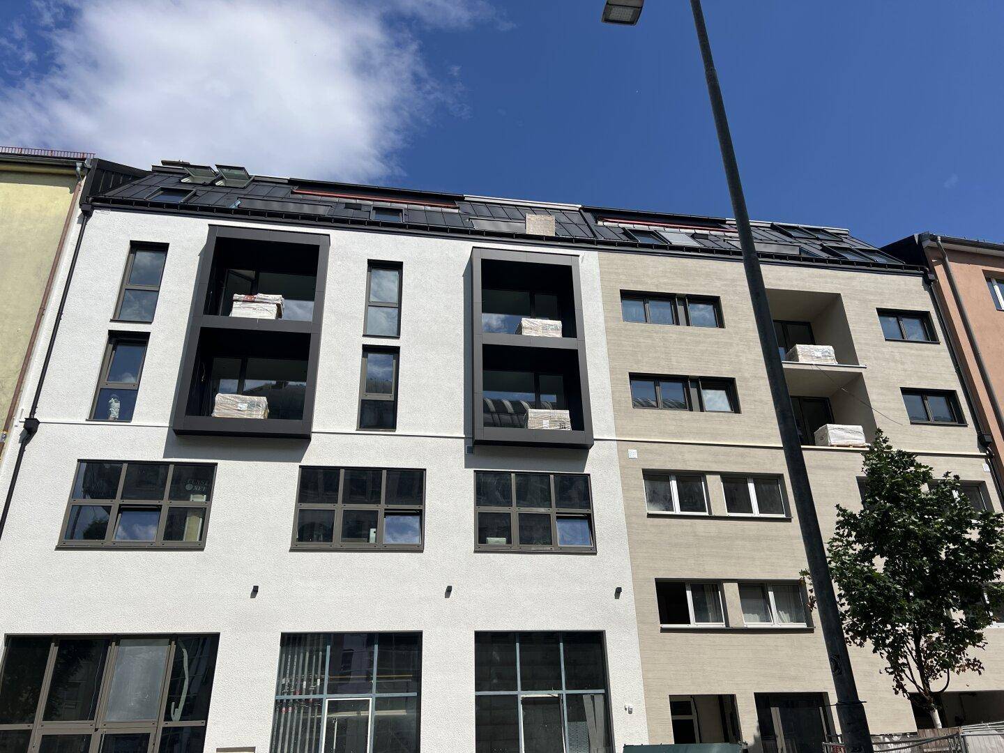 Moderne Fassade eines Neubaus mit großen Fenstern und Balkonen in städtischer Umgebung.