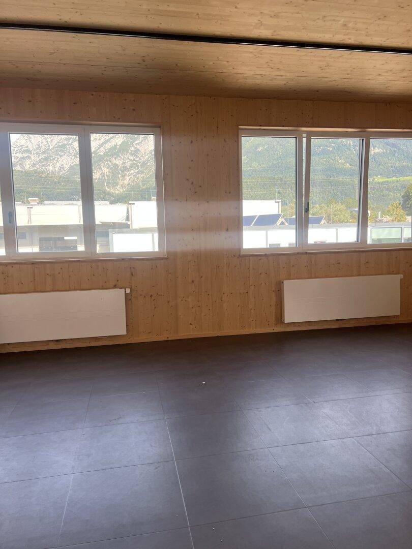 Heller Raum mit dunklem Fliesenboden, Holzwänden und -decke, bietet einen weiten Blick auf die umliegenden Berge.