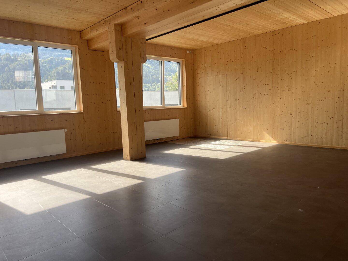 Geräumiger Raum mit dunklem Fliesenboden, Holzwänden und -decke, durchflutet von natürlichem Licht mit Bergblick.