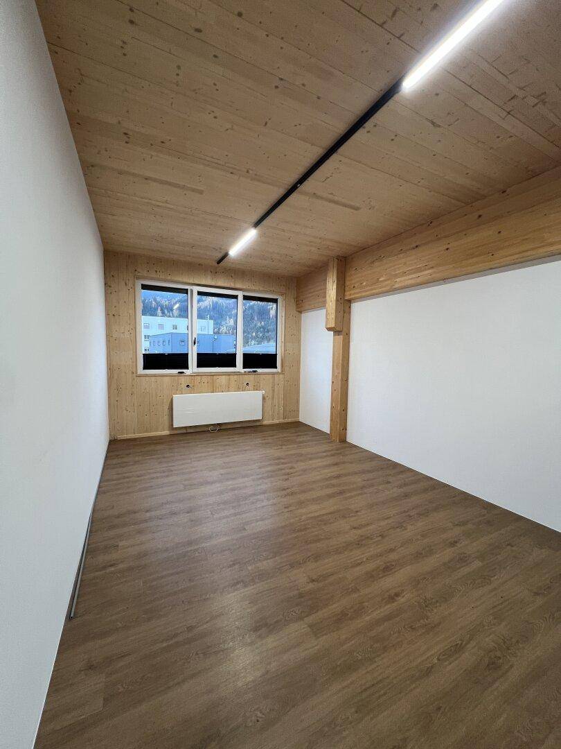 Heller Innenraum mit Holzwänden und -decke, Laminatboden und großen Fenstern, die viel Tageslicht hereinlassen.
