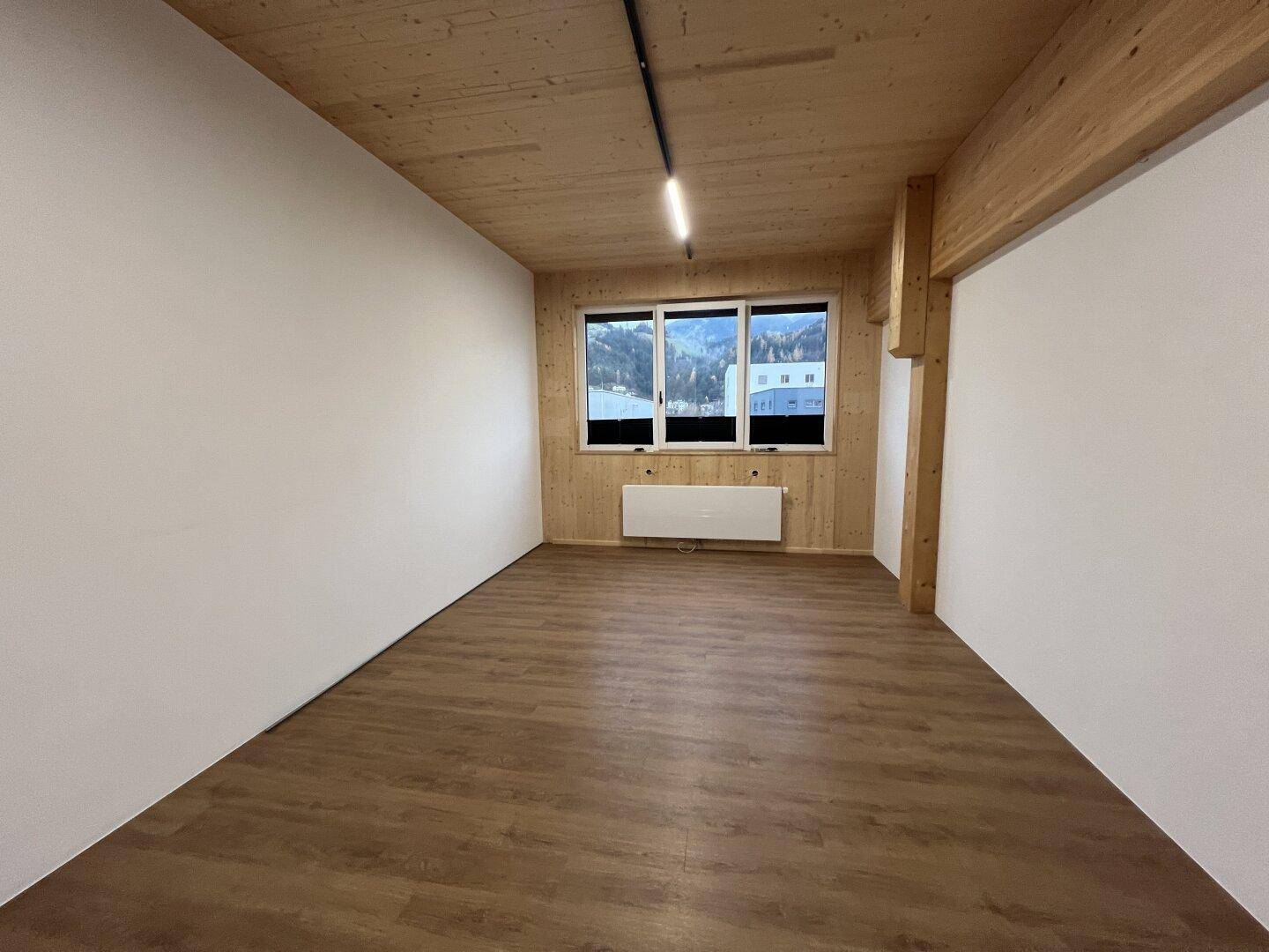 Heller Raum mit Holzwänden und -decke, Laminatboden und Fenstern mit Blick auf die Natur und möglicherweise Wasser.