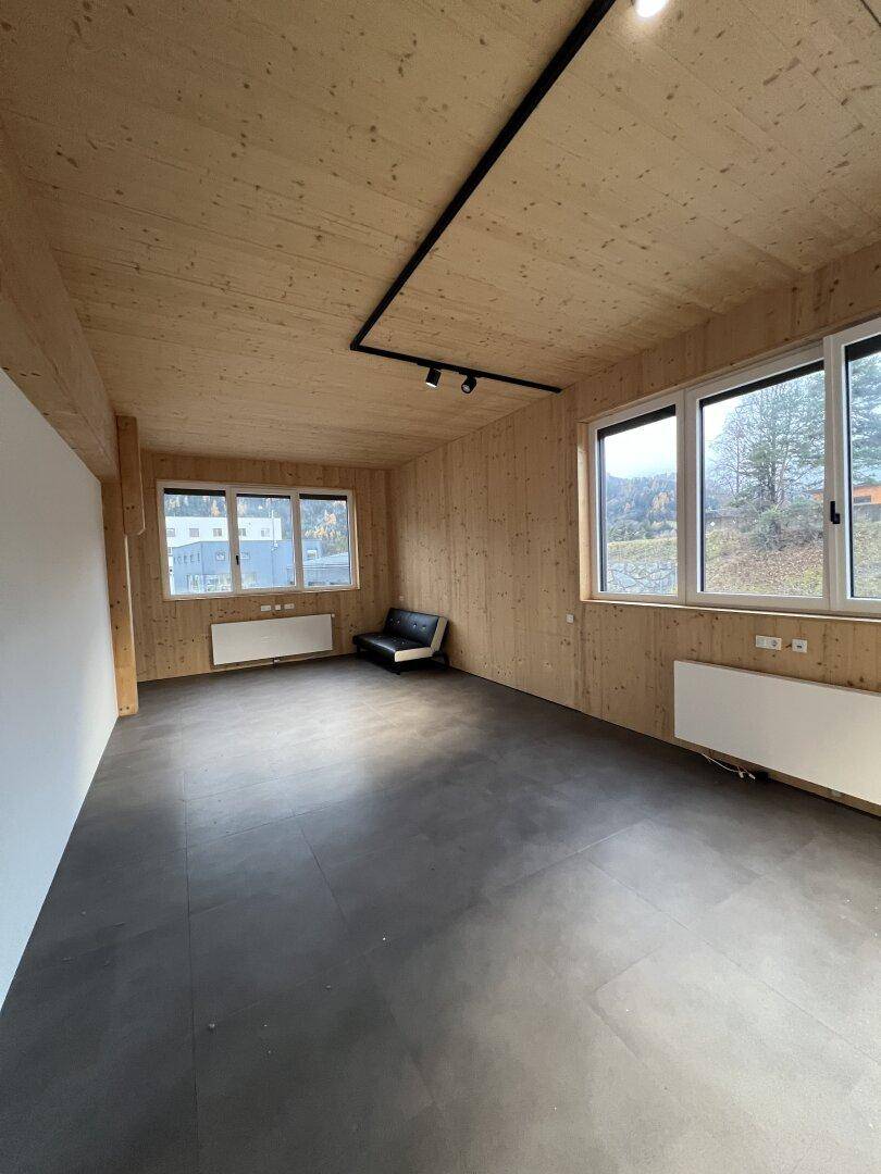 Geräumiger Raum mit Holzelementen, dunklem Fliesenboden und einem kleinen Sofa, bietet einen Blick ins Grüne.