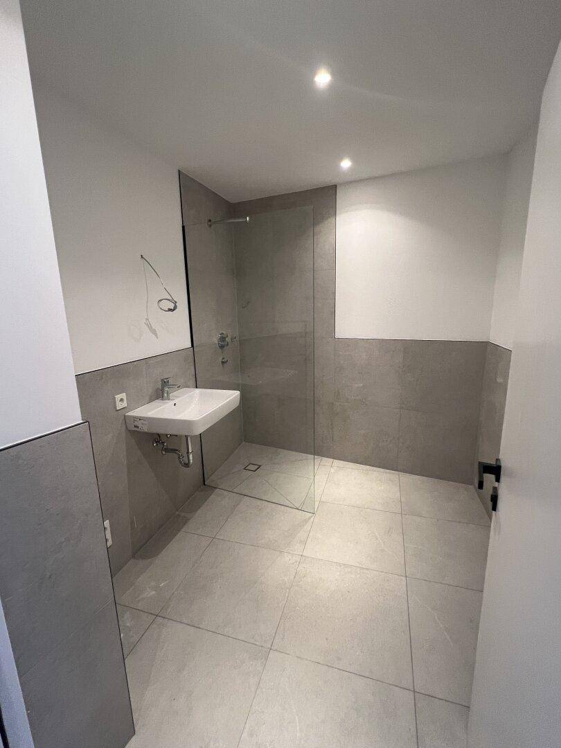 Modernes Badezimmer mit grauen Fliesen, ebenerdiger Dusche und einem einzelnen Waschbecken.