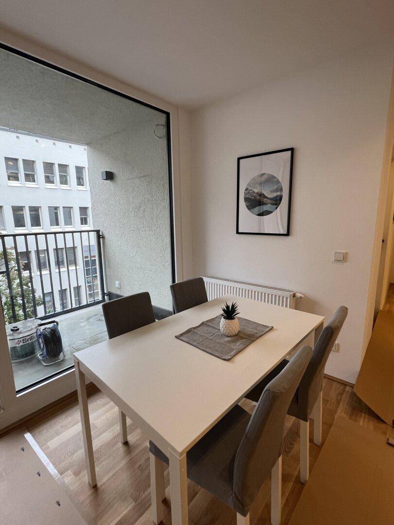 Heller Essbereich mit Holzboden, modernem Esstisch und Zugang zu einem Balkon.