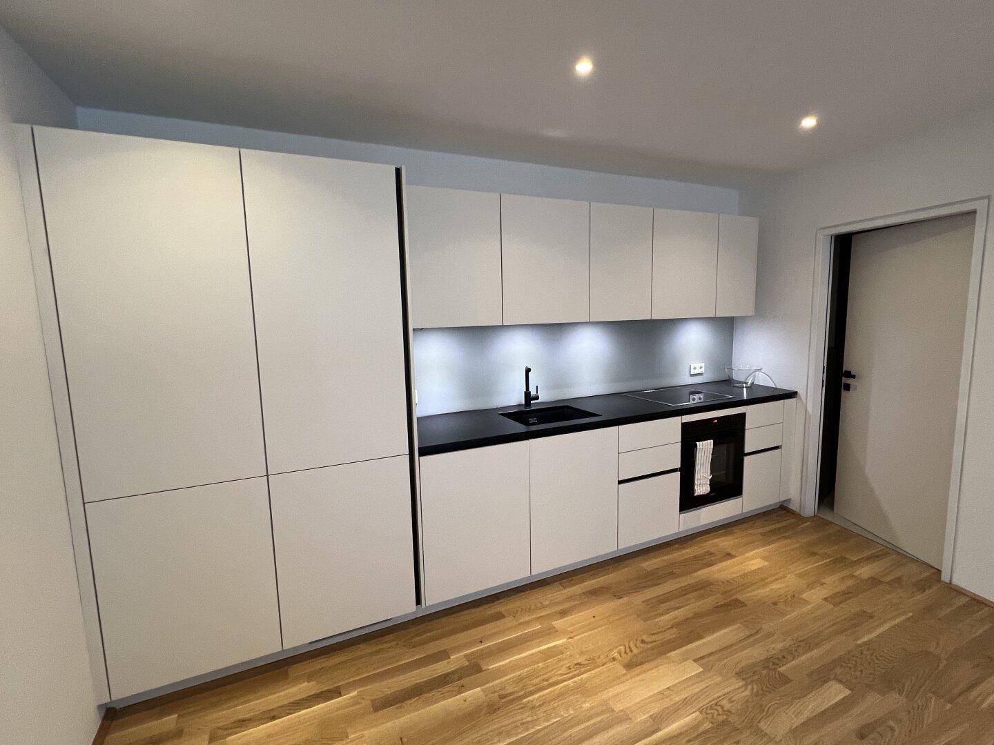 Moderne Einbauküche mit weißen Schränken, schwarzer Arbeitsplatte und integrierten Geräten.