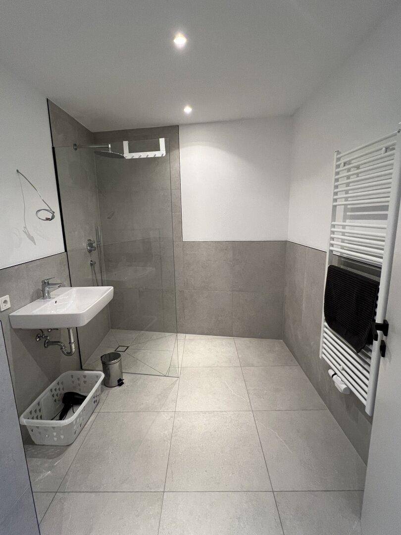 Modernes Badezimmer mit grauen Fliesen, ebenerdiger Dusche und beheiztem Handtuchhalter.