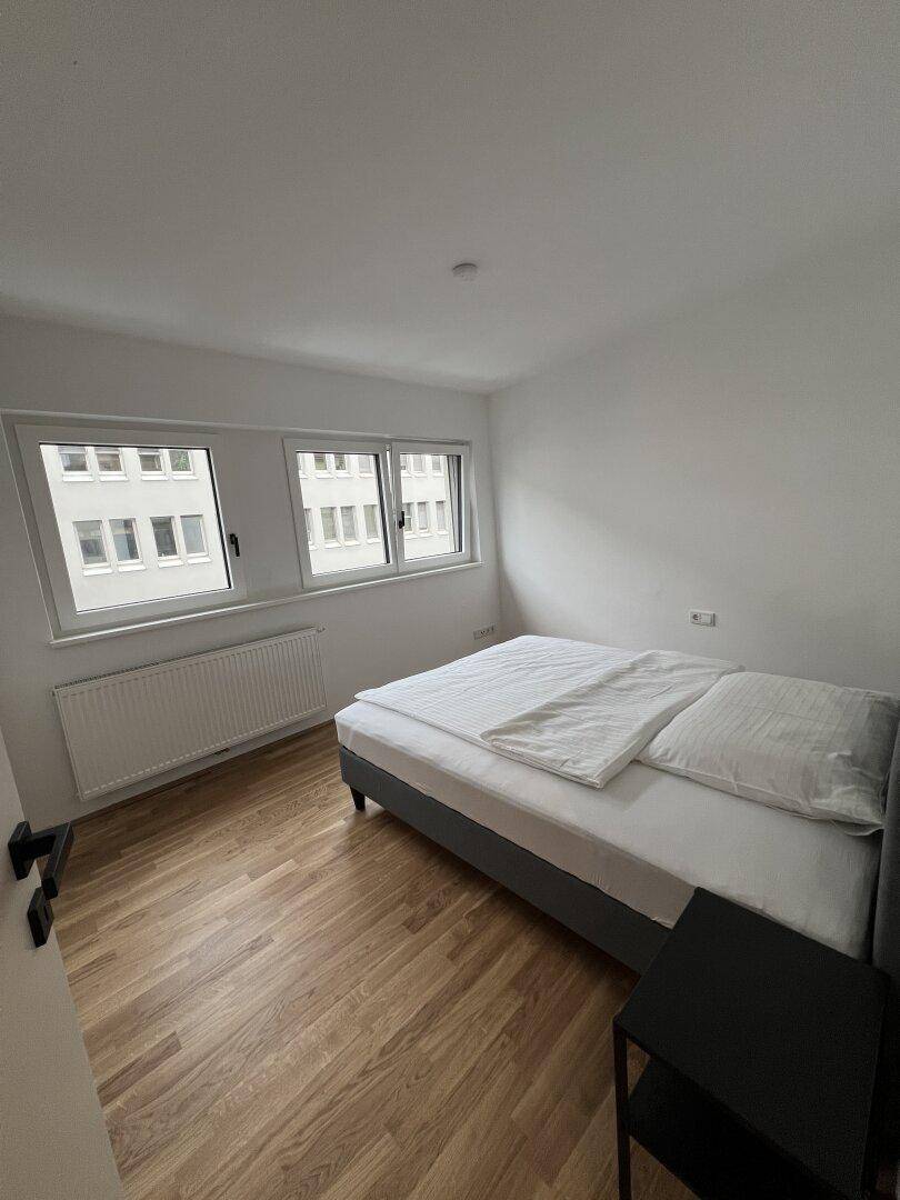 Helles Schlafzimmer mit Holzboden, Doppelbett und großen Fenstern.