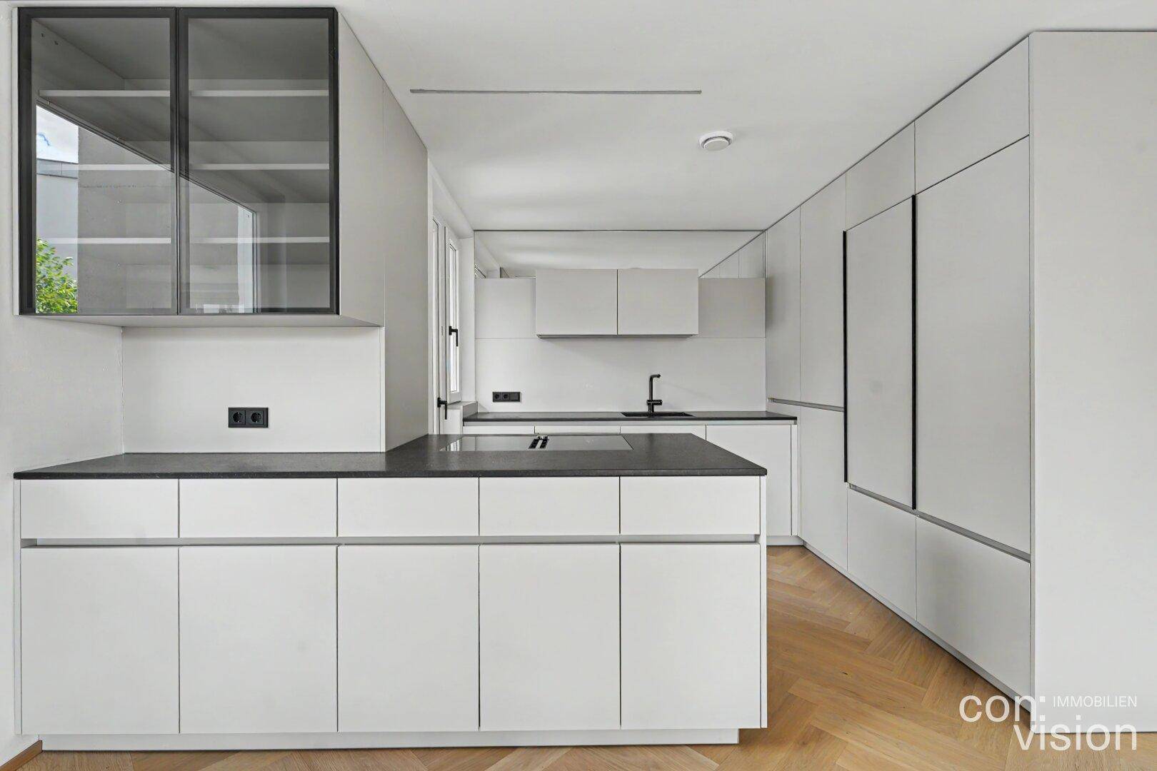 Helle, moderne Küche mit weißen Schränken, dunkler Arbeitsplatte und Glasvitrine.