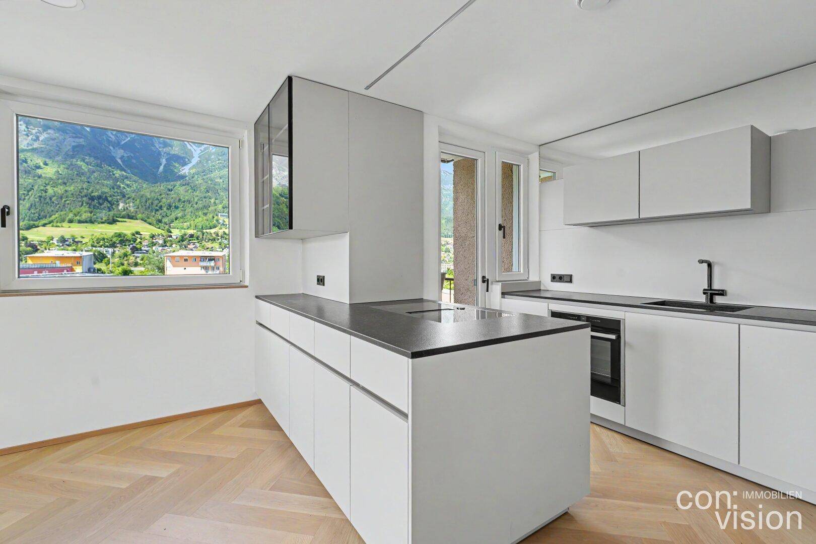 Helle Küche mit Kücheninsel, integriertem Kochfeld und Zugang zu einem Balkon mit Bergblick.