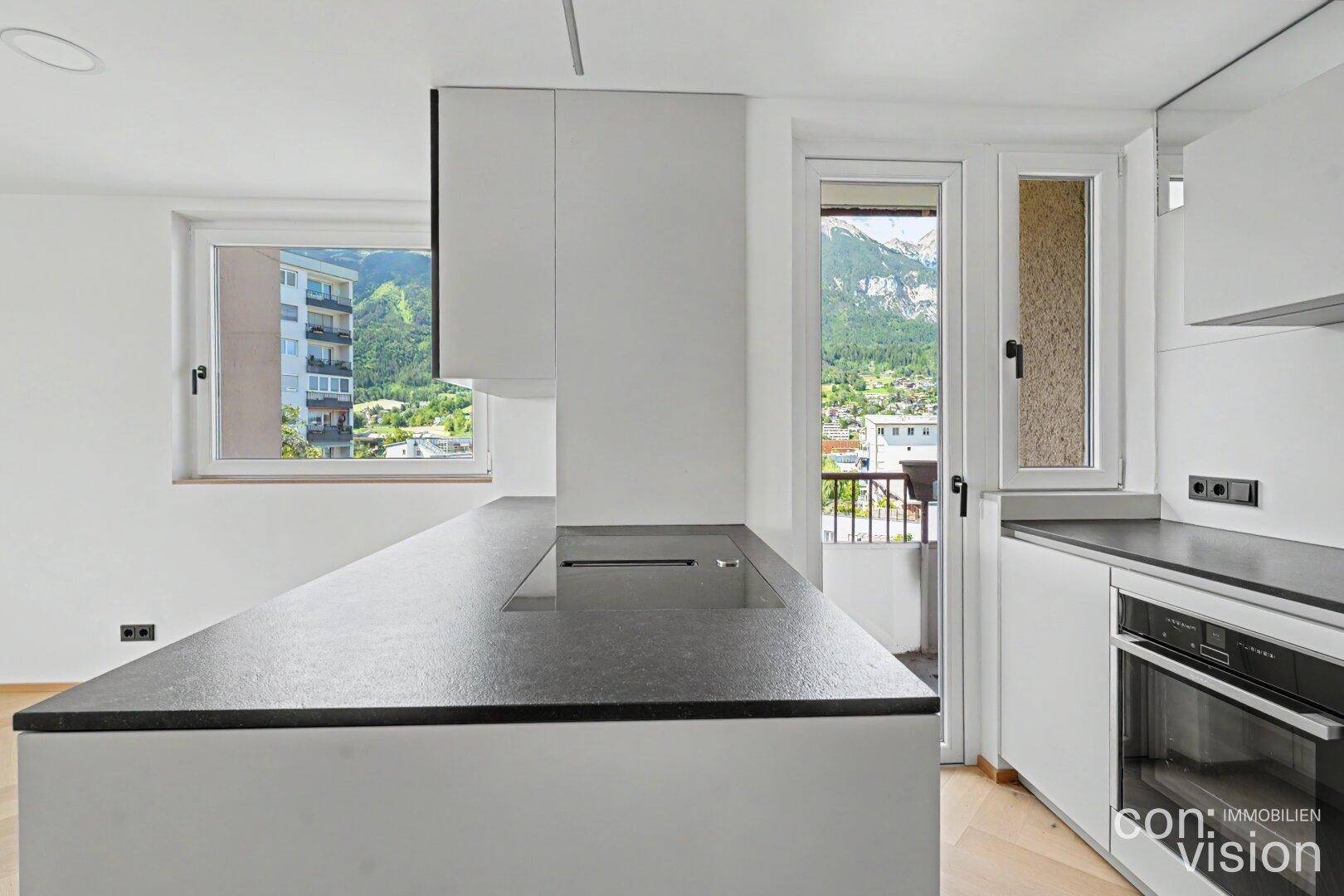 Detailansicht der modernen Kücheninsel mit Kochfeld und Blick auf die Berge vom Balkon.