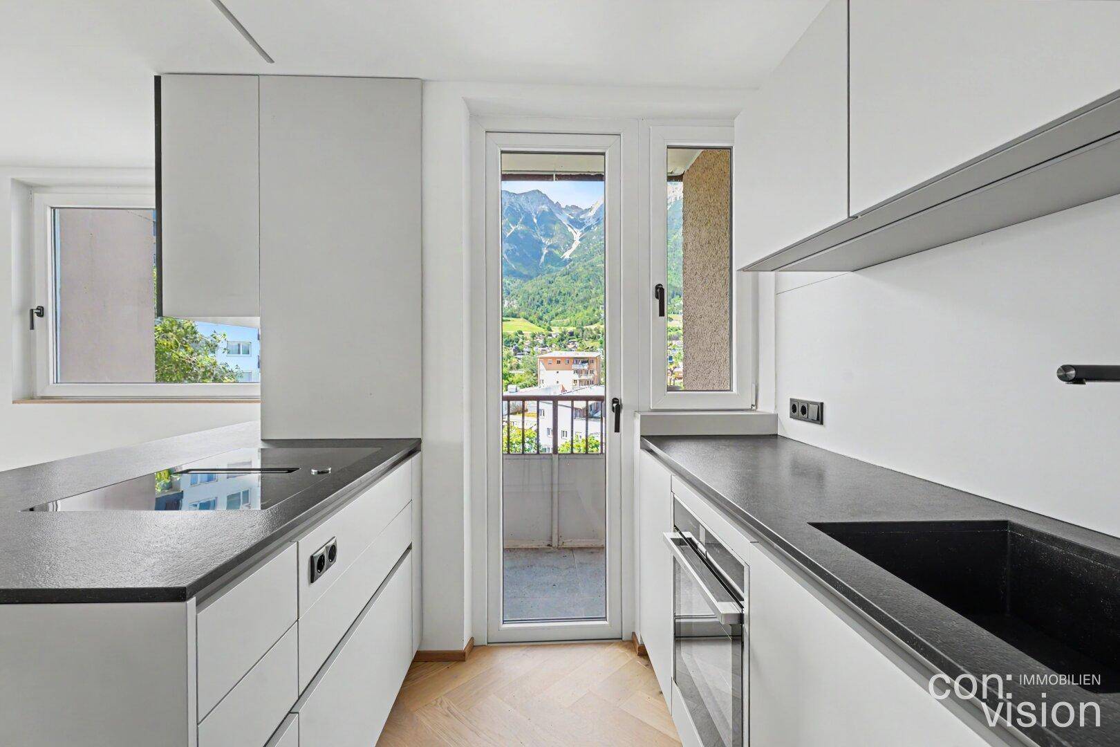 Moderne Küche mit dunkler Spüle, Backofen und Zugang zu einem französischen Balkon mit Bergblick.