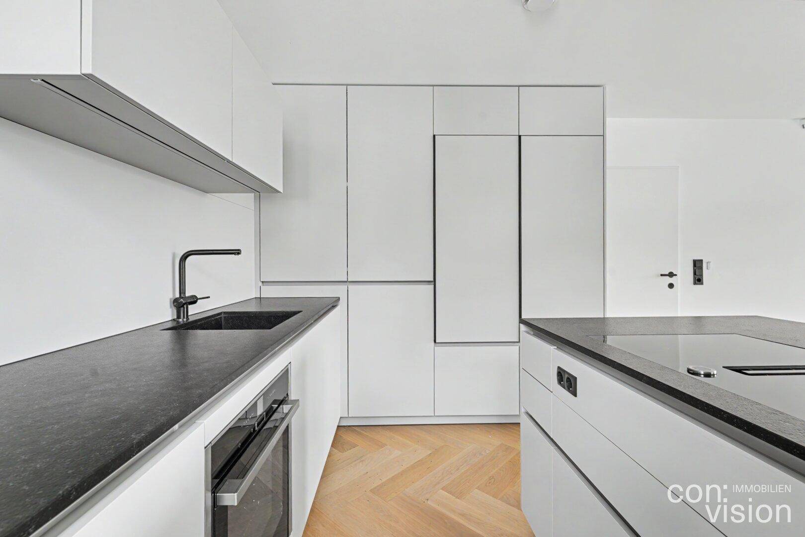 Geräumige, moderne Küche mit weißen Schränken, dunklen Arbeitsplatten und integrierten Geräten.