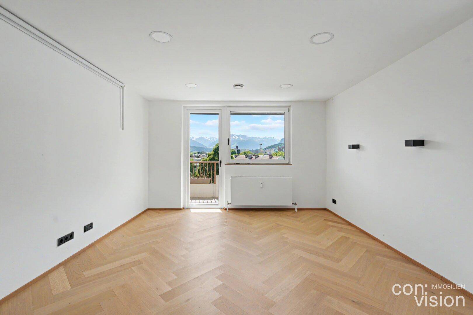 Helles Wohnzimmer mit Fischgrätparkett, Zugang zum Balkon und weitem Bergblick.