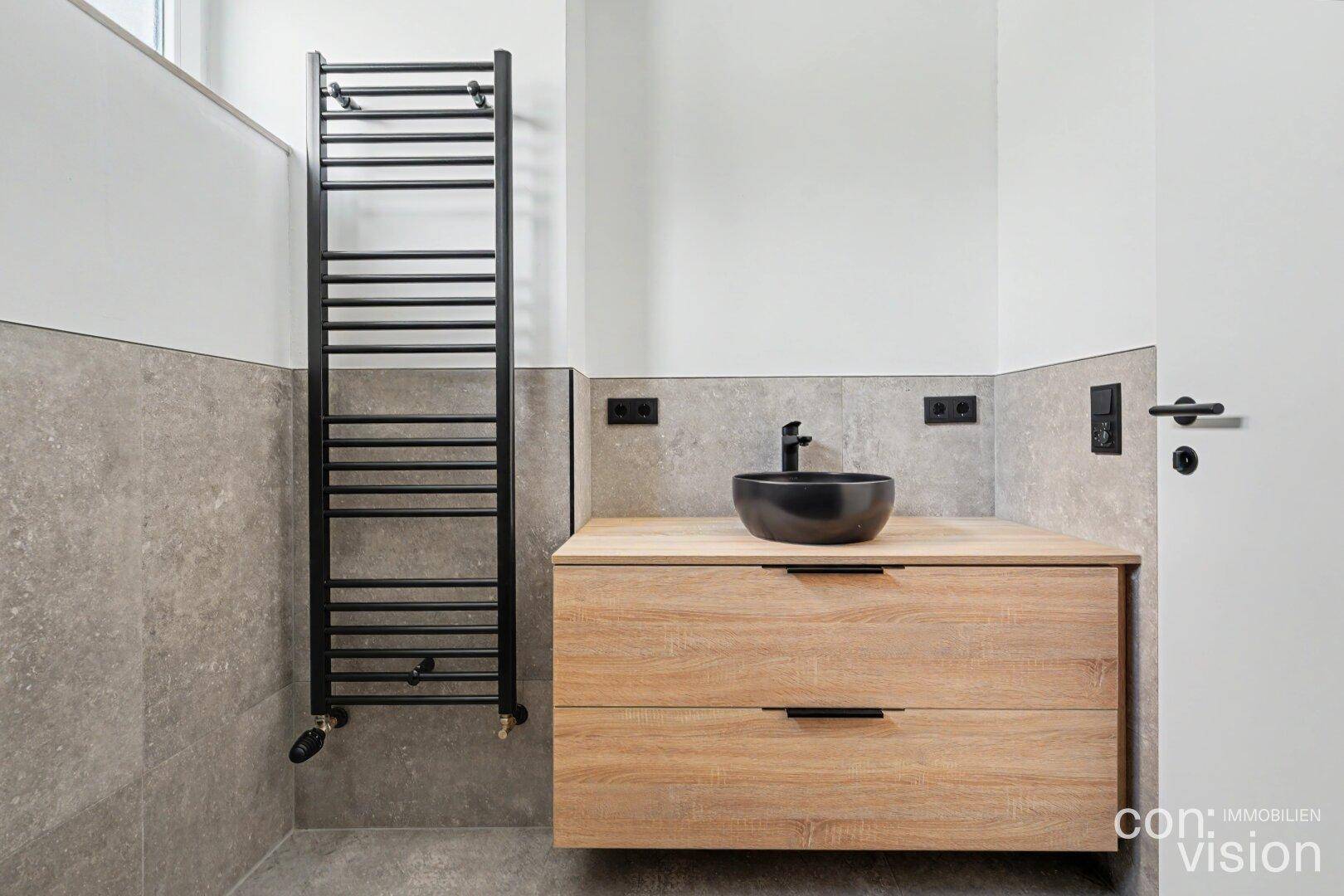 Modernes Badezimmer mit Holzwaschtisch, schwarzem Waschbecken und beheiztem Handtuchhalter.