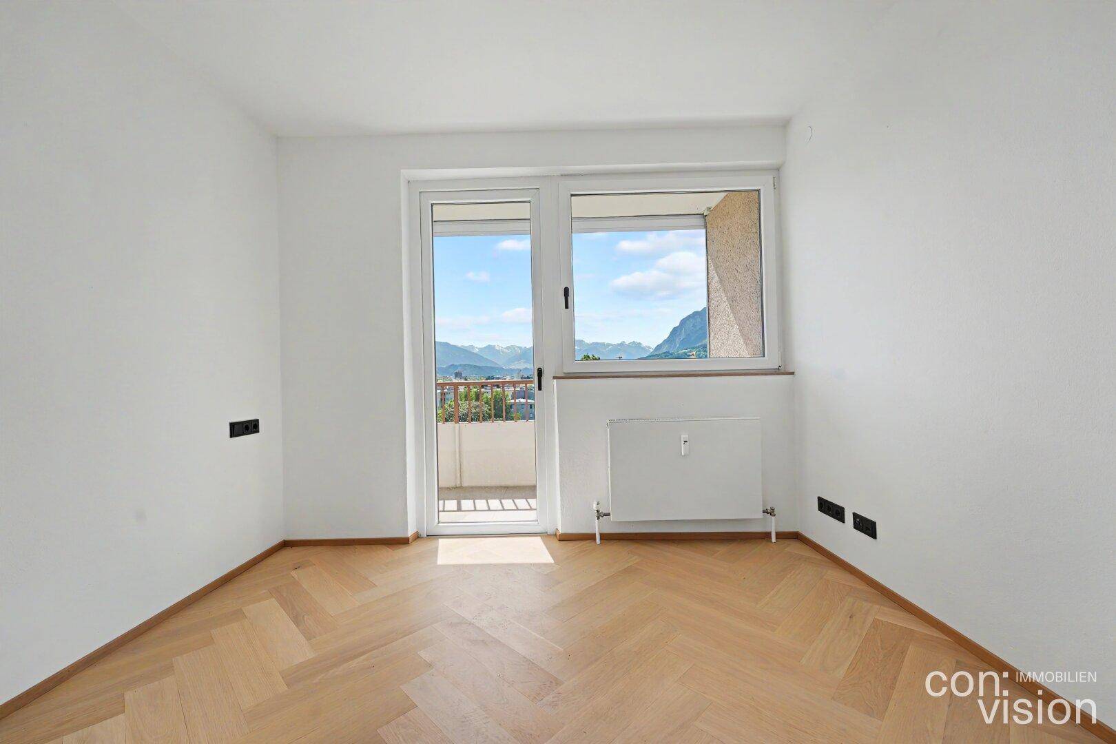 Helles Schlafzimmer mit Fischgrätparkett, Balkonzugang und weitem Bergblick.
