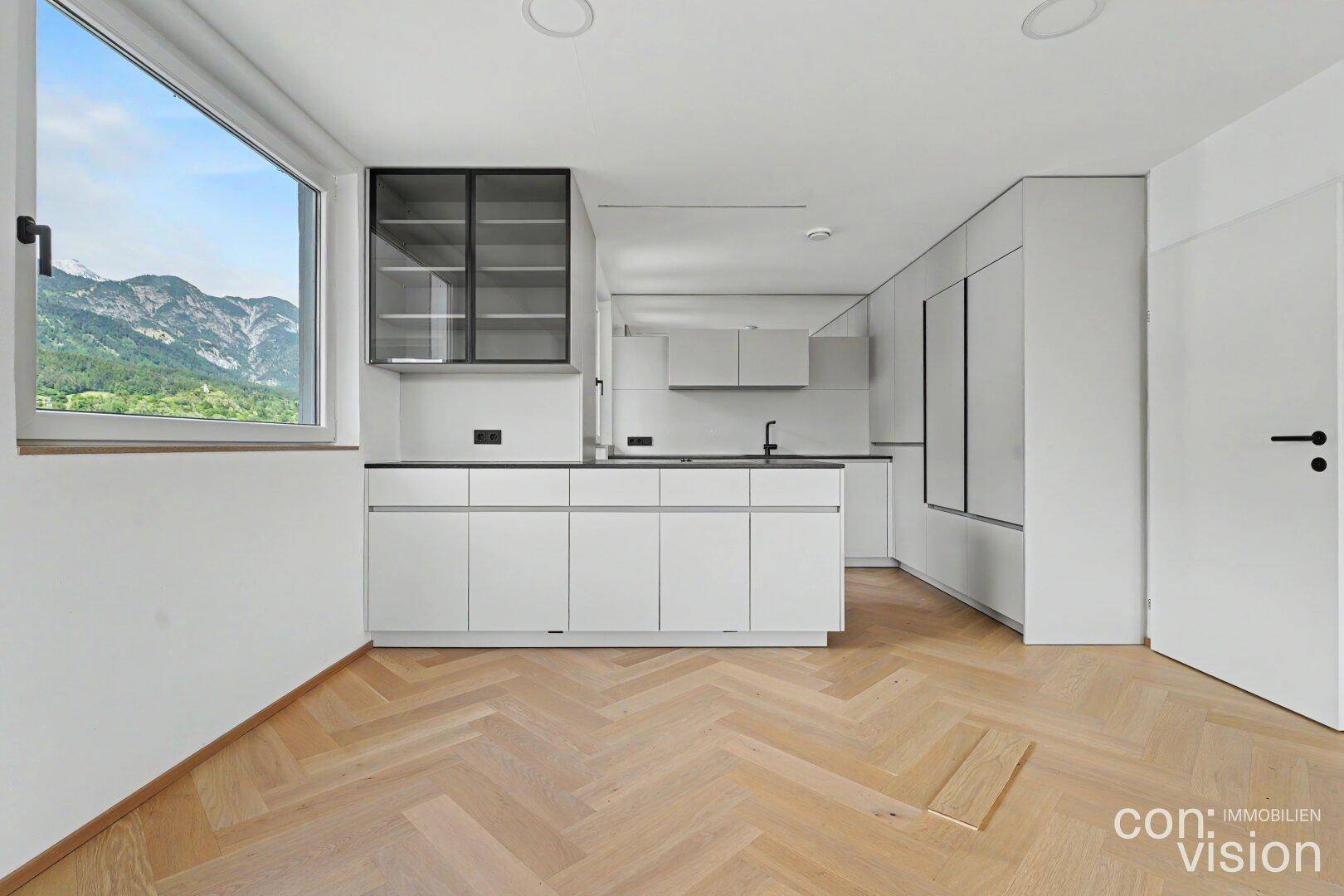 Moderne Küche mit weißen Schränken, dunkler Arbeitsplatte und Bergblick durch das Fenster.