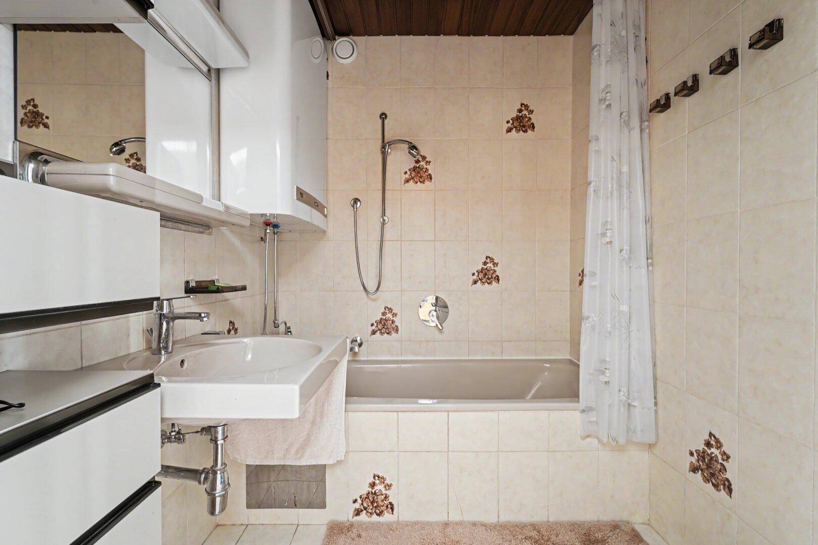 Badezimmer mit Badewanne, Waschbecken und beigefarbenen Fliesen mit floralen Mustern.