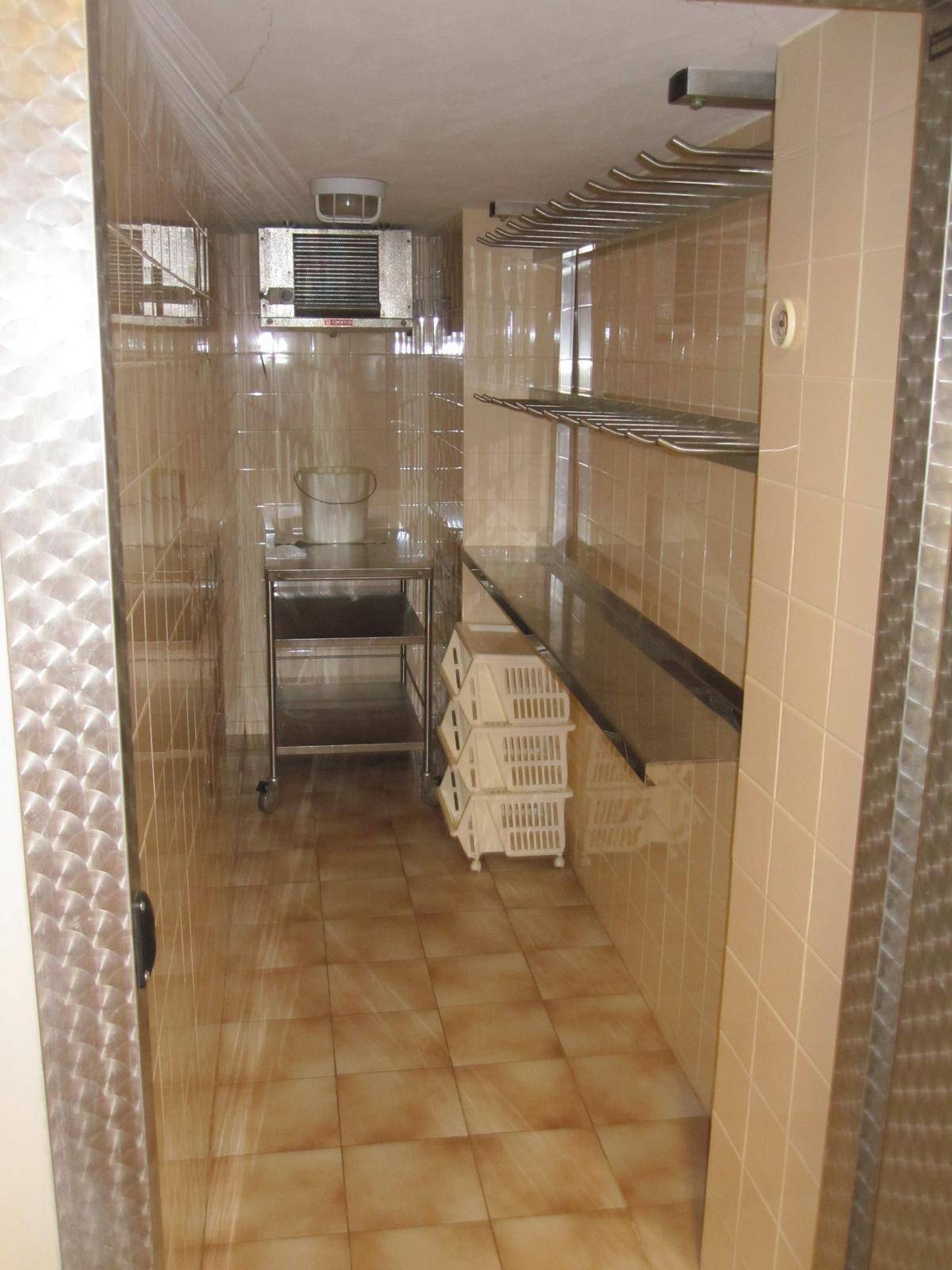 Gefliester Kühlraum oder Vorratskammer mit Metallregalen und einer Kühleinheit an der Decke.