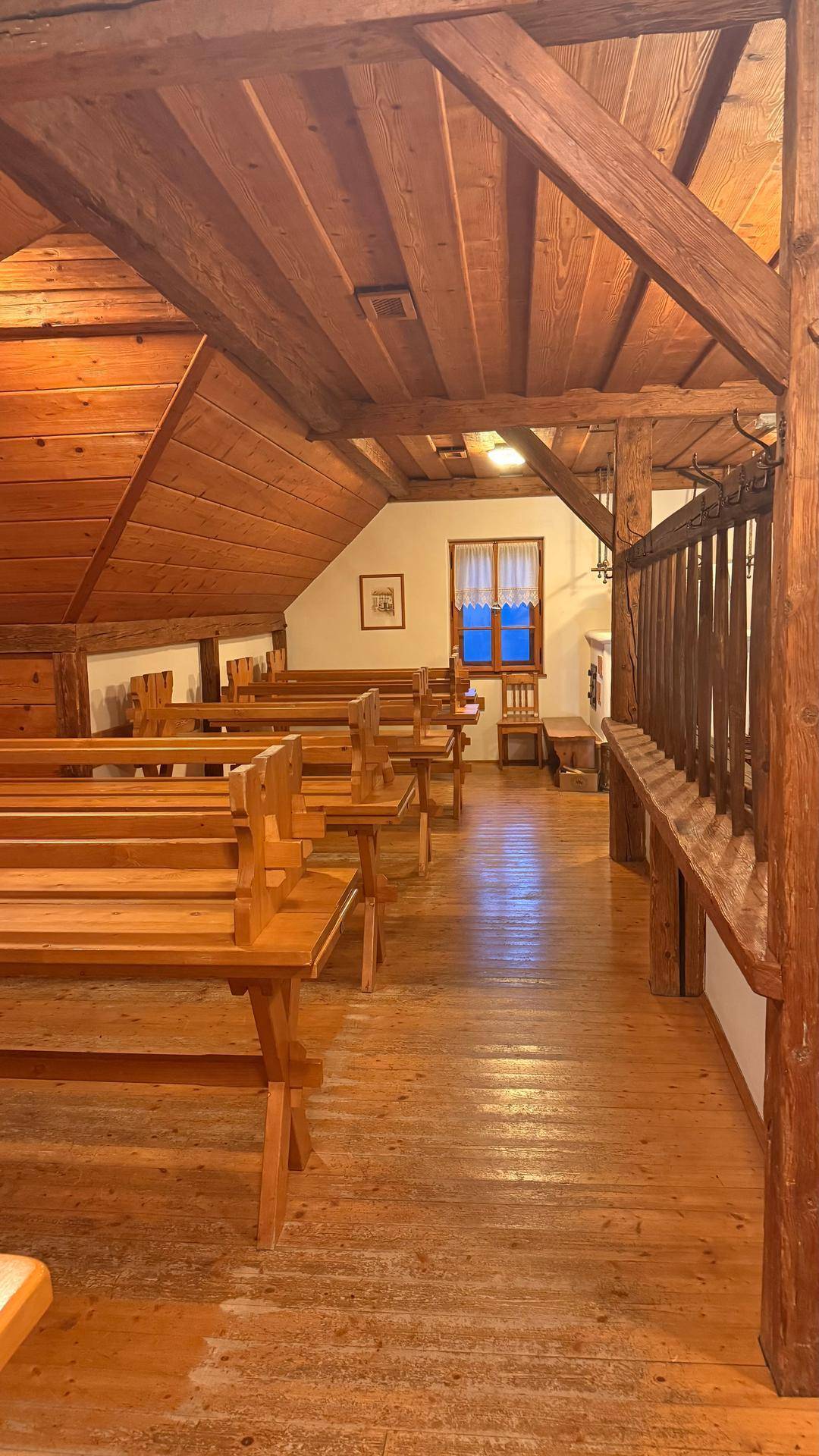 Geräumiger Dachgeschossraum mit Holzbalken, schräger Decke und vielen Holzbänken und Tischen.
