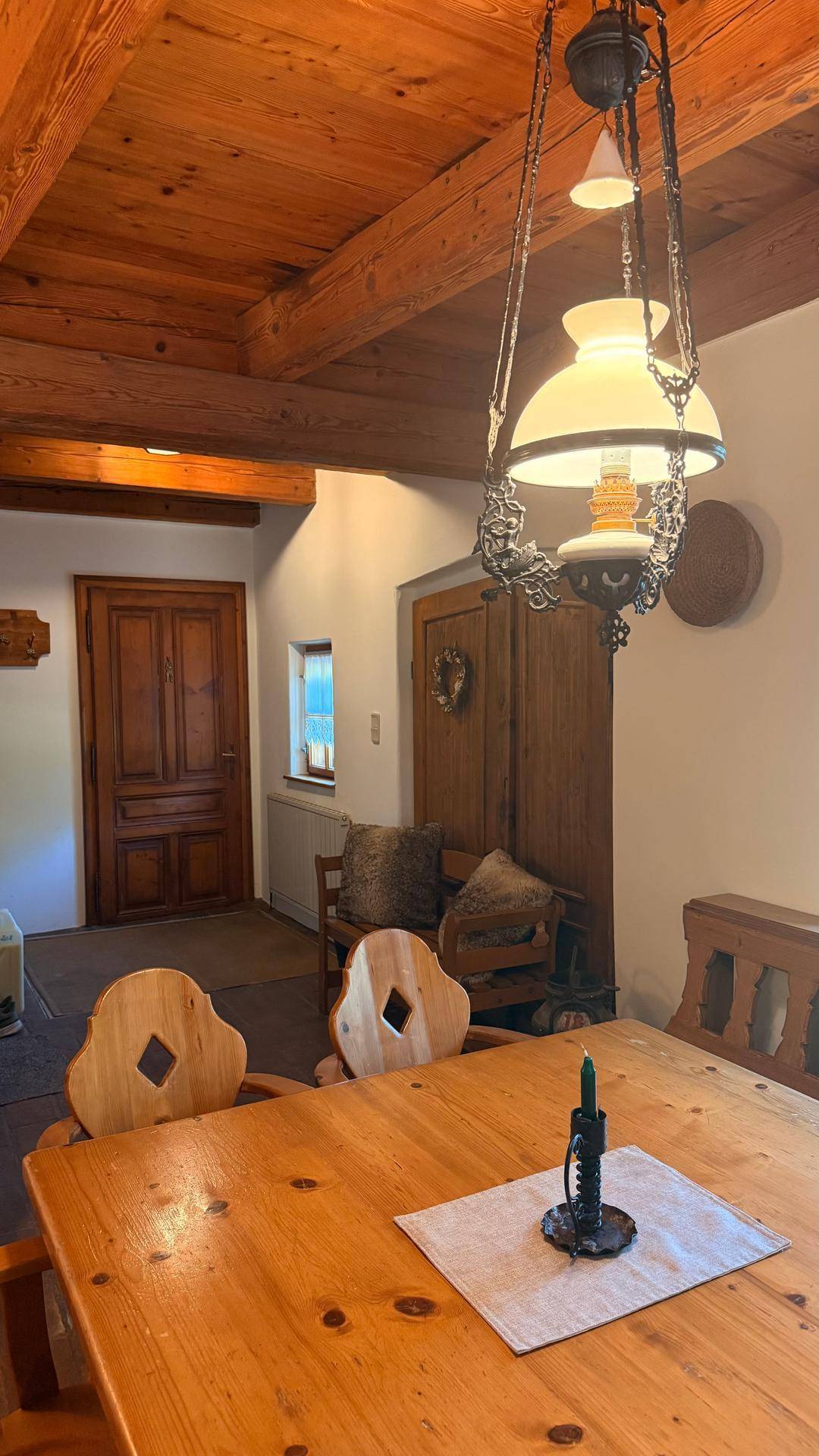 Rustikaler Essbereich mit Holzbalkendecke und Blick auf einen Flur mit traditioneller Holztür.