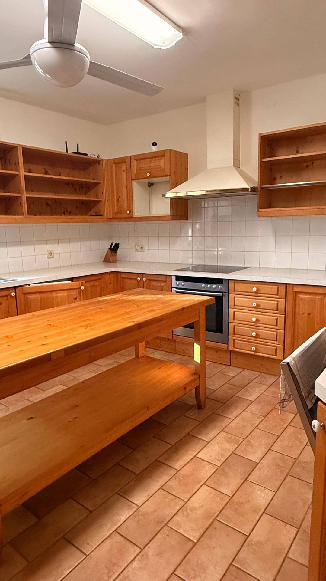 Geräumige Küche mit Holzschränken, Fliesenboden, einer Kücheninsel und einem Deckenventilator.