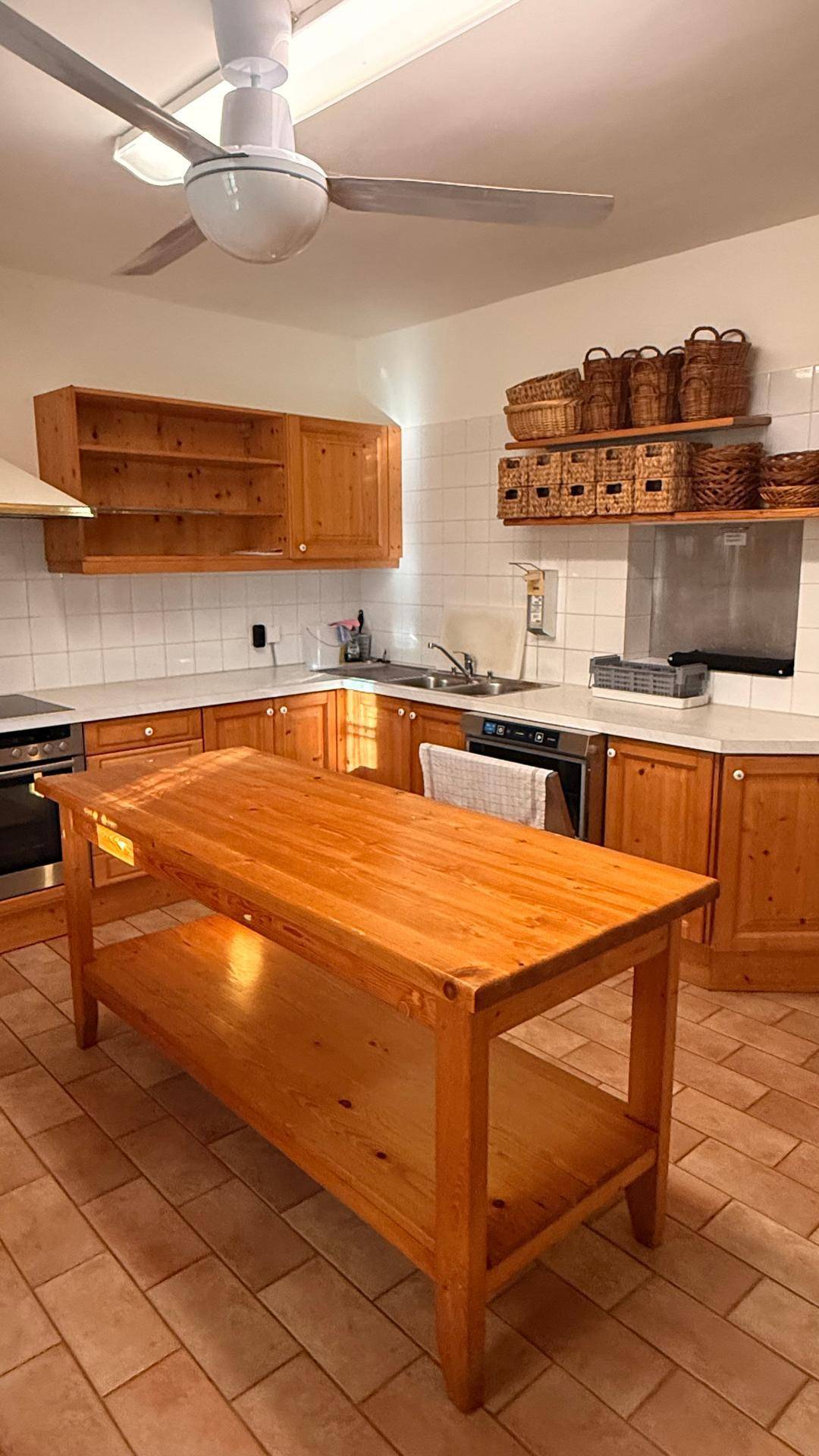Helle Küche mit Holzmöbeln, Fliesenboden, einer großen Kücheninsel und einem Deckenventilator.