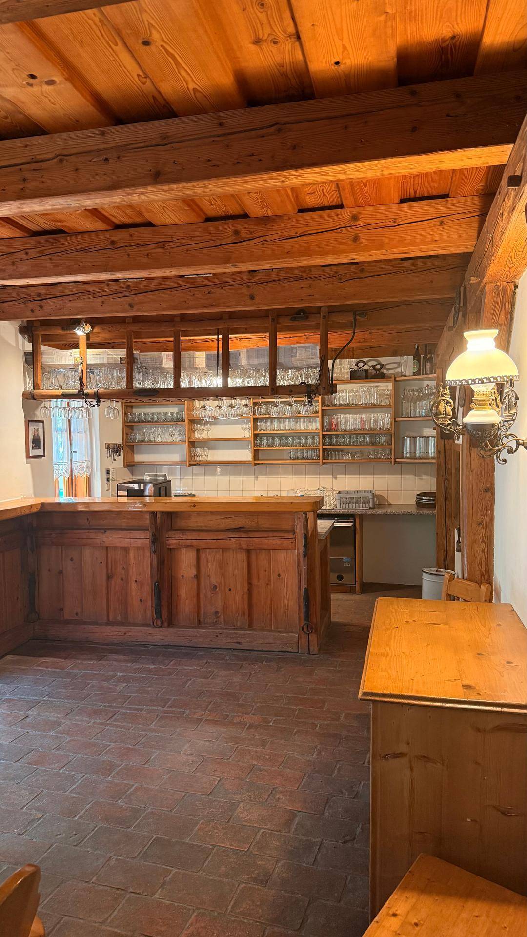 Rustikaler Barbereich mit Holzbalkendecke, Terrakottafliesen und einer Theke mit Glasregalen.