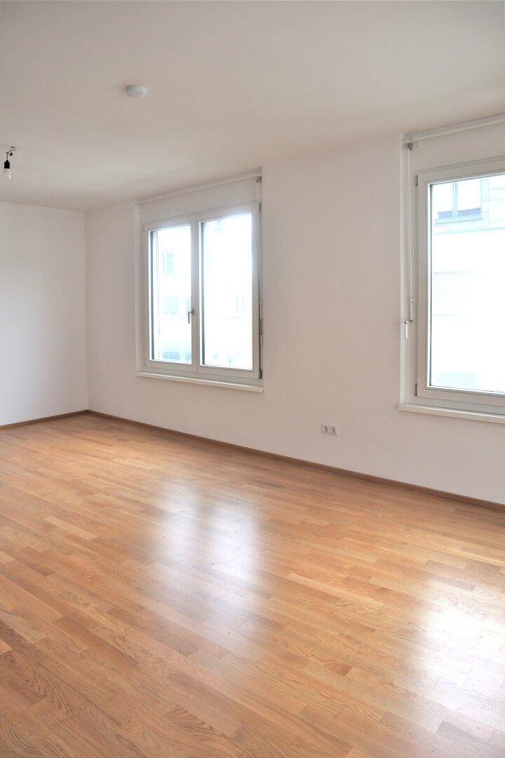 Geräumiges Wohnzimmer mit hellem Parkettboden und großen Fenstern.