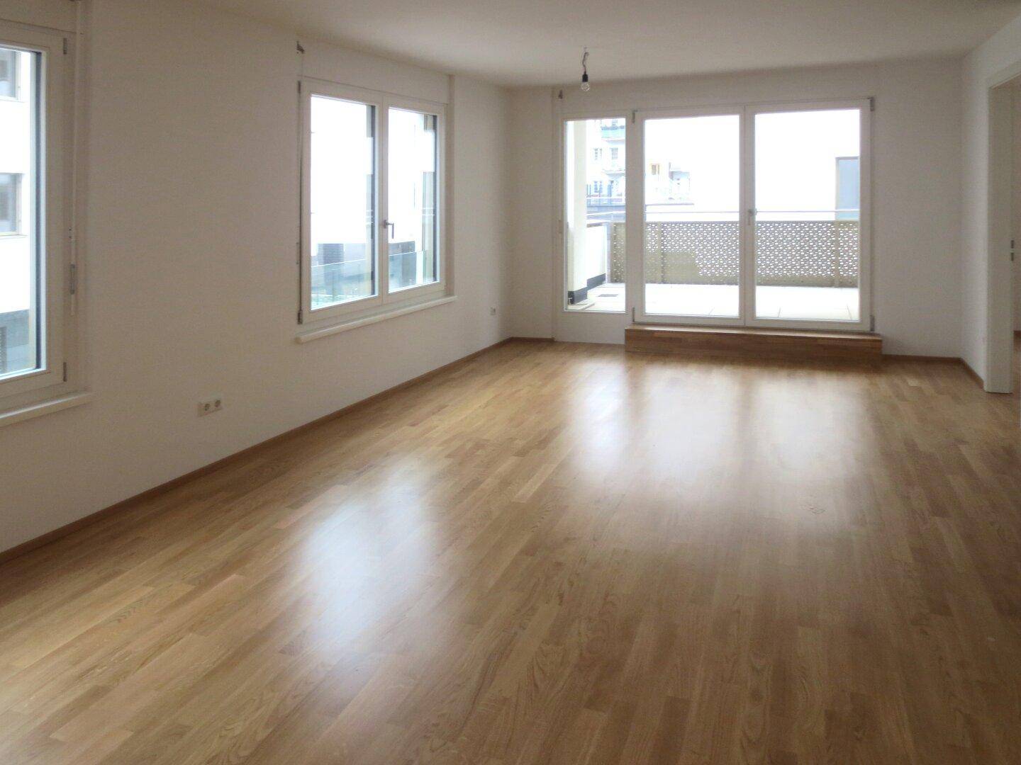 Helles Wohnzimmer mit Parkettboden und Zugang zu einem Balkon.