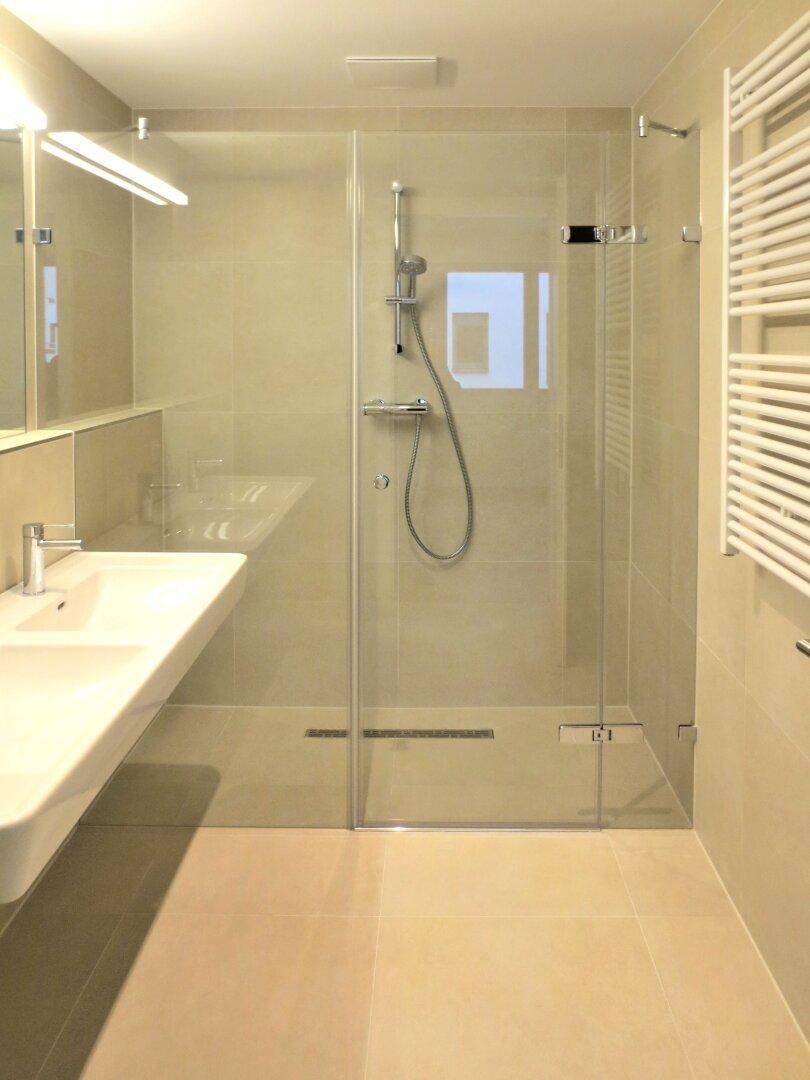 Helles Badezimmer mit ebenerdiger Dusche, Glaswand und beheiztem Handtuchhalter.