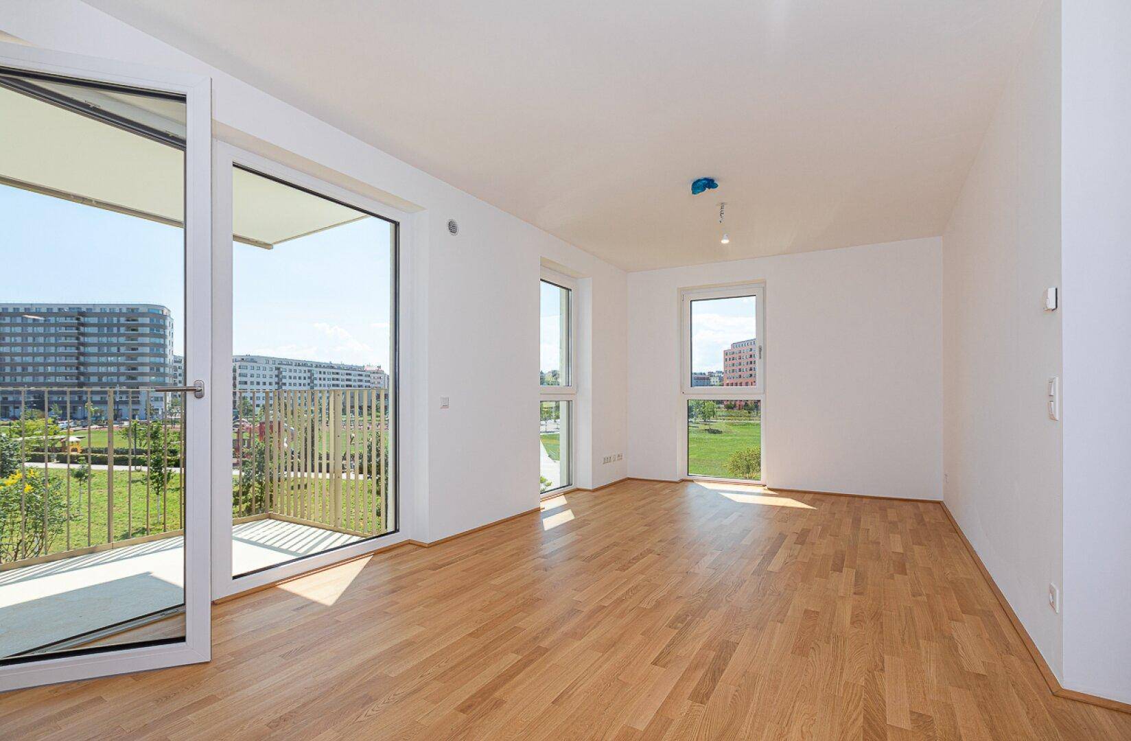 Lichtdurchfluteter Wohnraum mit Parkettboden, großen Fenstern und direktem Zugang zum Balkon.