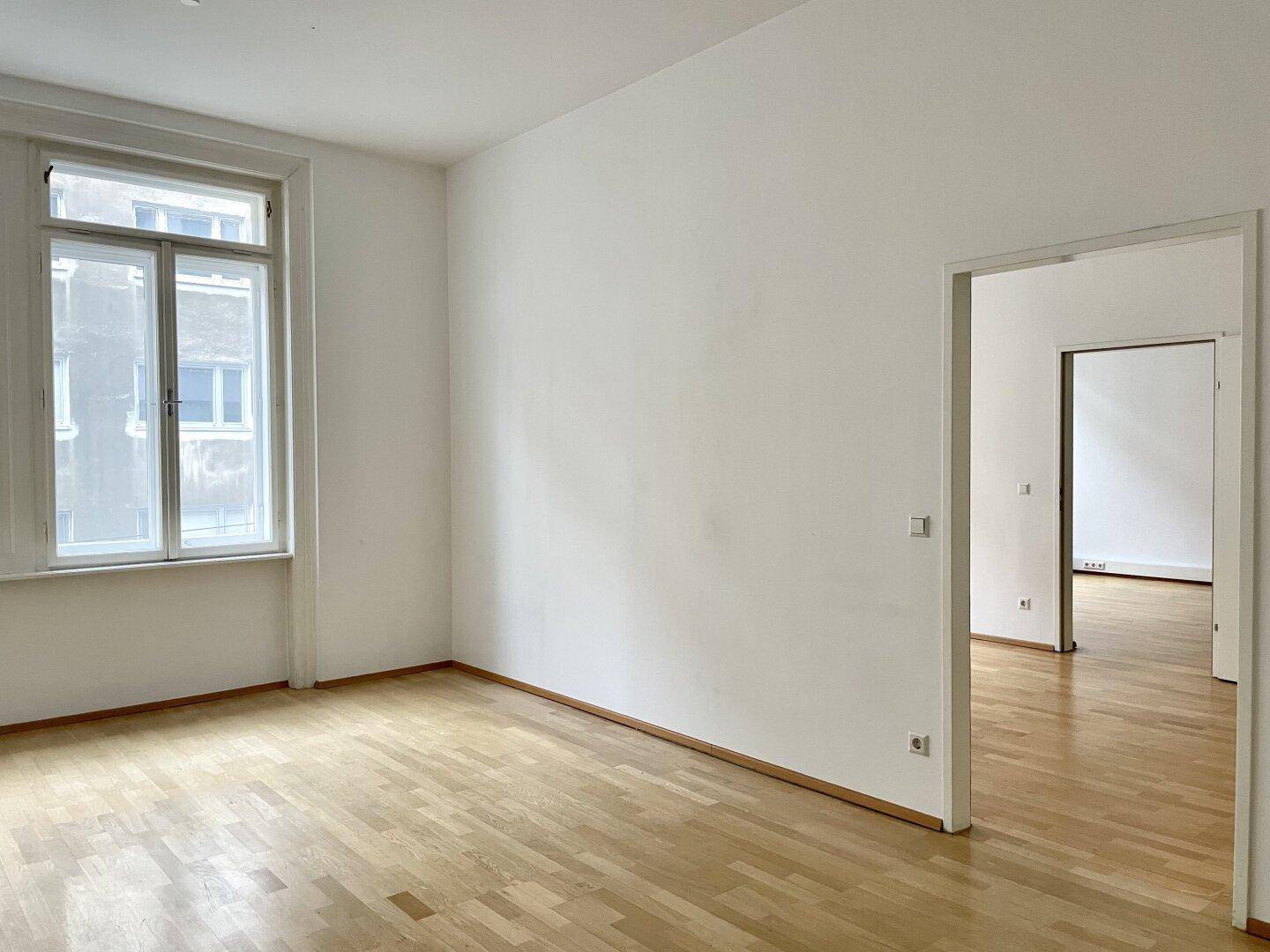 Geräumiger, heller Raum mit Holzboden und Blick auf die umliegenden Gebäude.