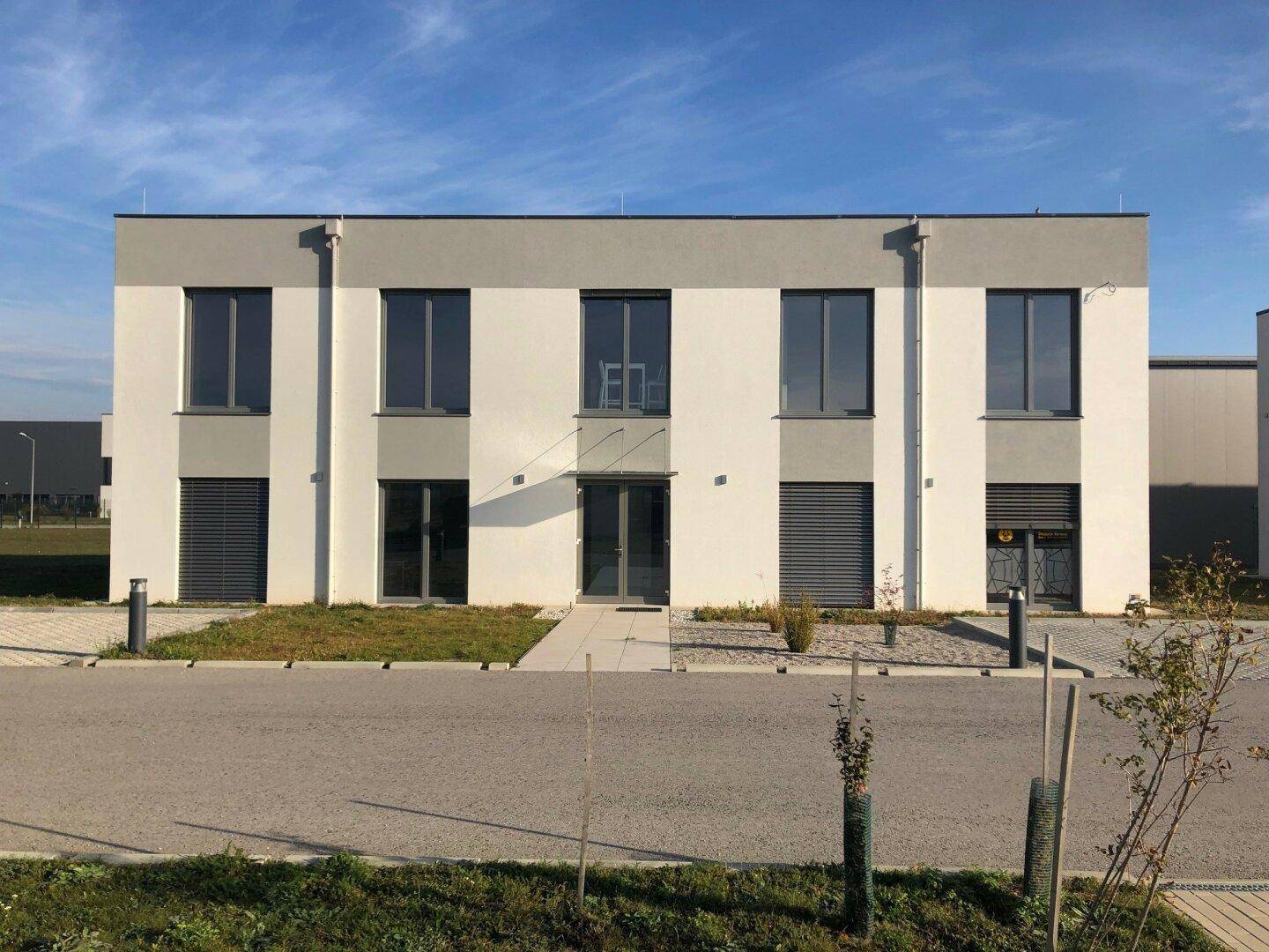 Moderne Bürogebäude-Fassade mit großen Fenstern und Jalousien unter blauem Himmel.