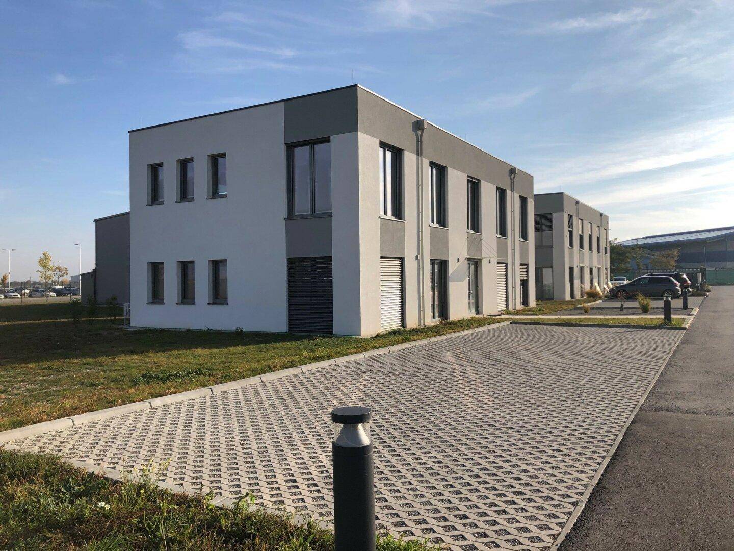 Seitenansicht eines modernen Bürokomplexes mit gepflastertem Parkplatz und Grünflächen.
