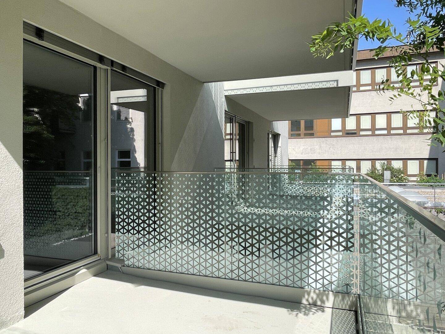 Moderner Balkon mit Glasgeländer und geometrischem Muster, bietet einen Blick auf die Umgebung.