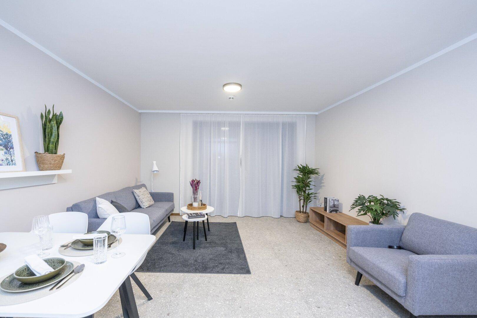 Heller Wohn- und Essbereich mit modernen Möbeln, großem Fenster und hellem Fliesenboden.