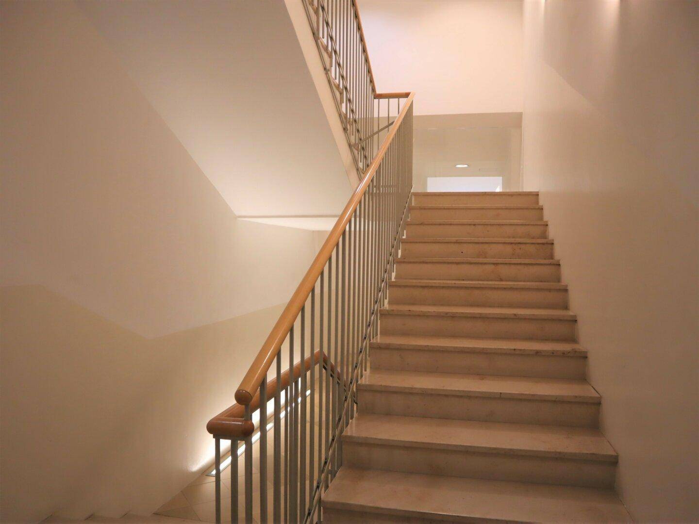 Modernes Treppenhaus mit Marmorstufen und Metallgeländer, gut beleuchtet und in sehr gepflegtem Zustand.